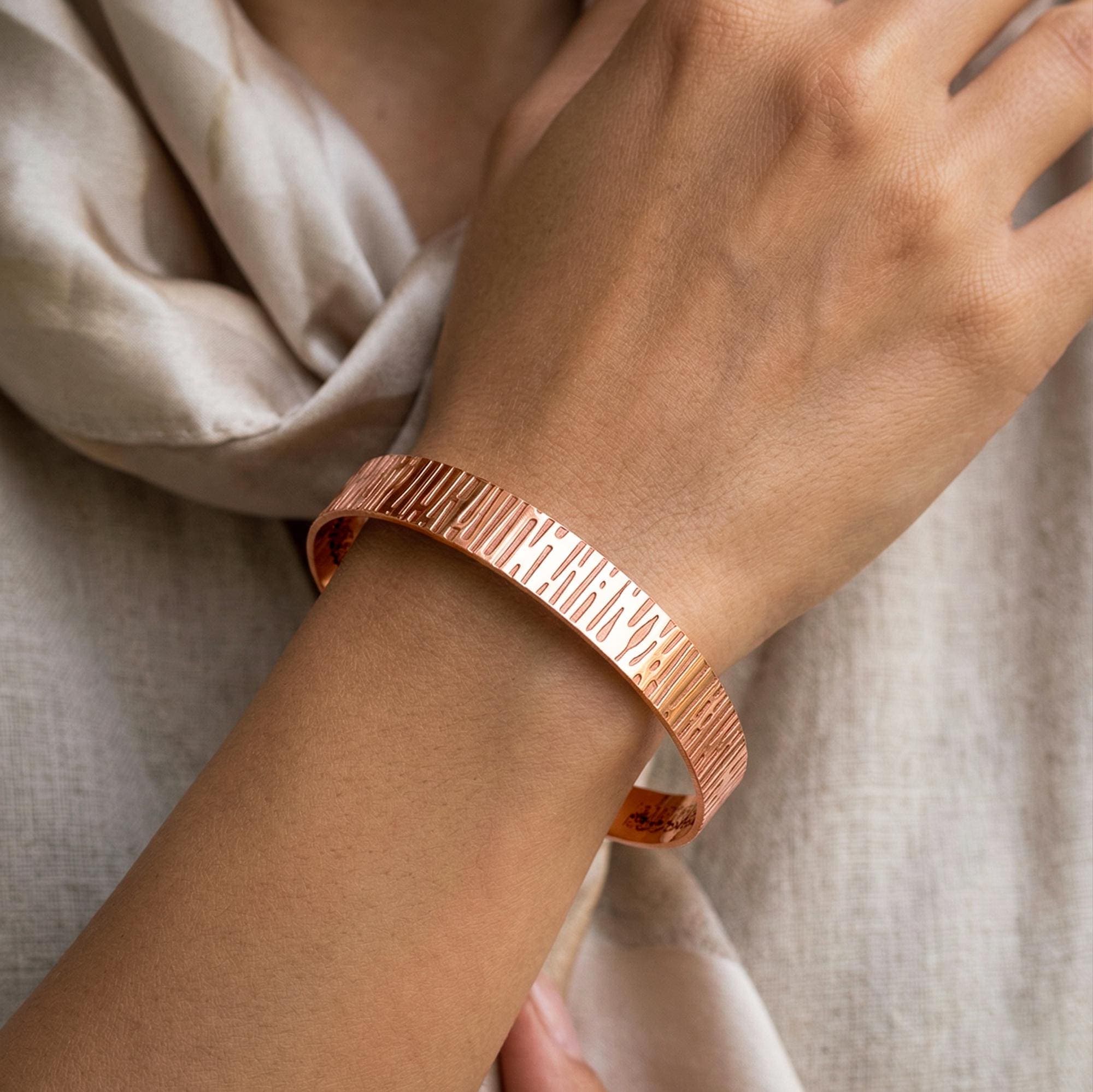 Minimalist 8mm wide Ayatul Kursi engraved inside, copper cuff, boutique handcrafted jewelry featuring a unique hammered texture and slim profile for daily wear on a womans arm close-up photo