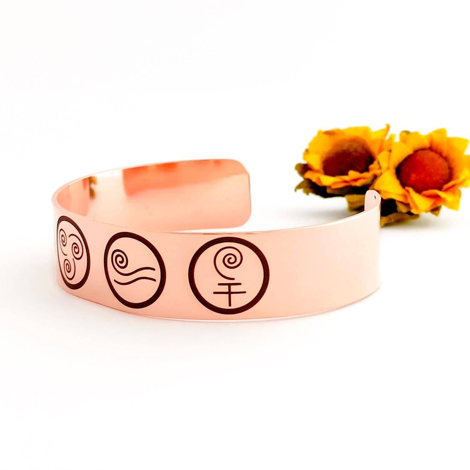 A copper bracelet with five engraved symbols, representing the four elements of earth, air, fire, and water