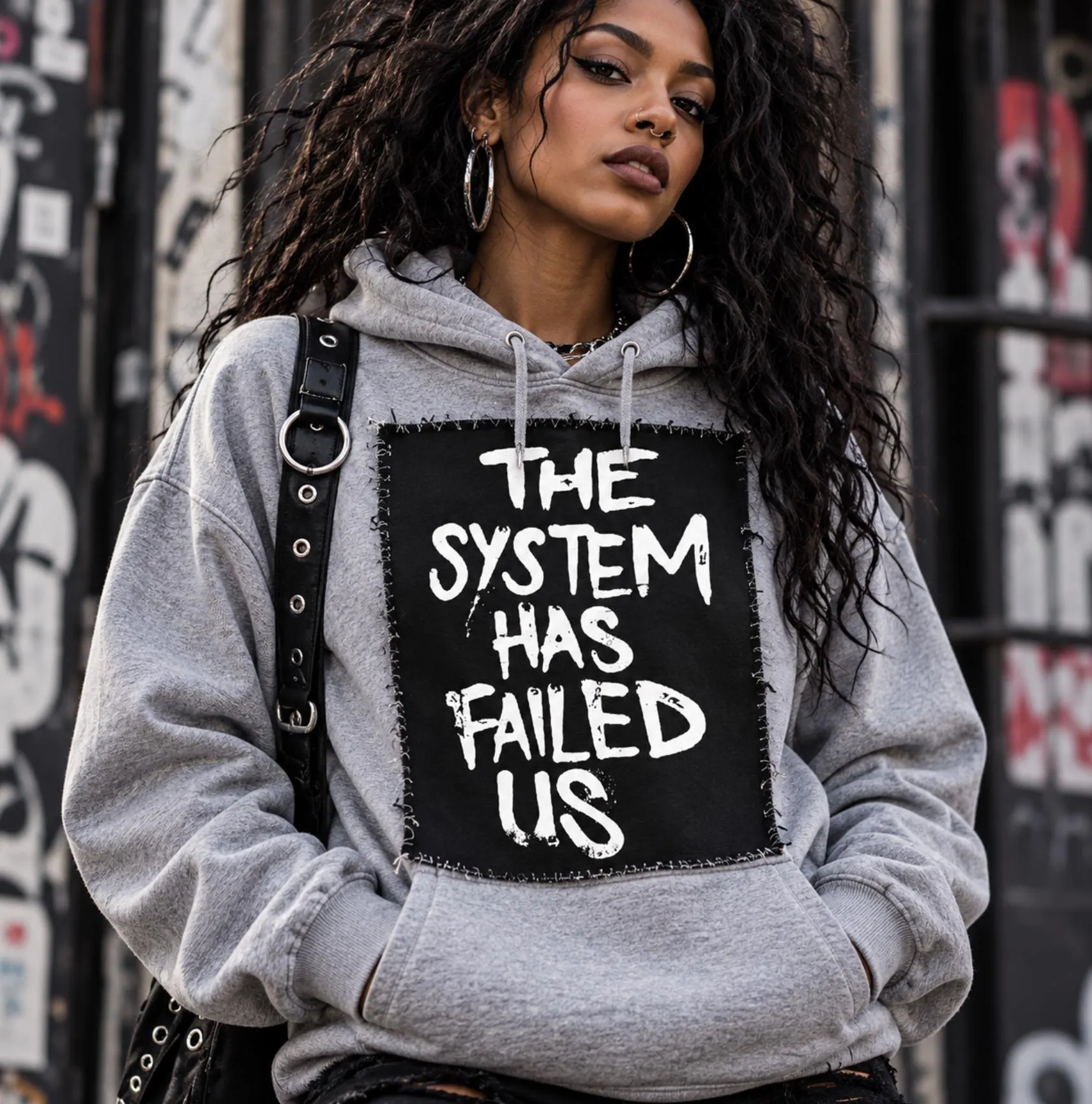 Black female punk model wearing a gray hoodie with oversized The System Has Failed Us black and white protest patch sewn on the front.