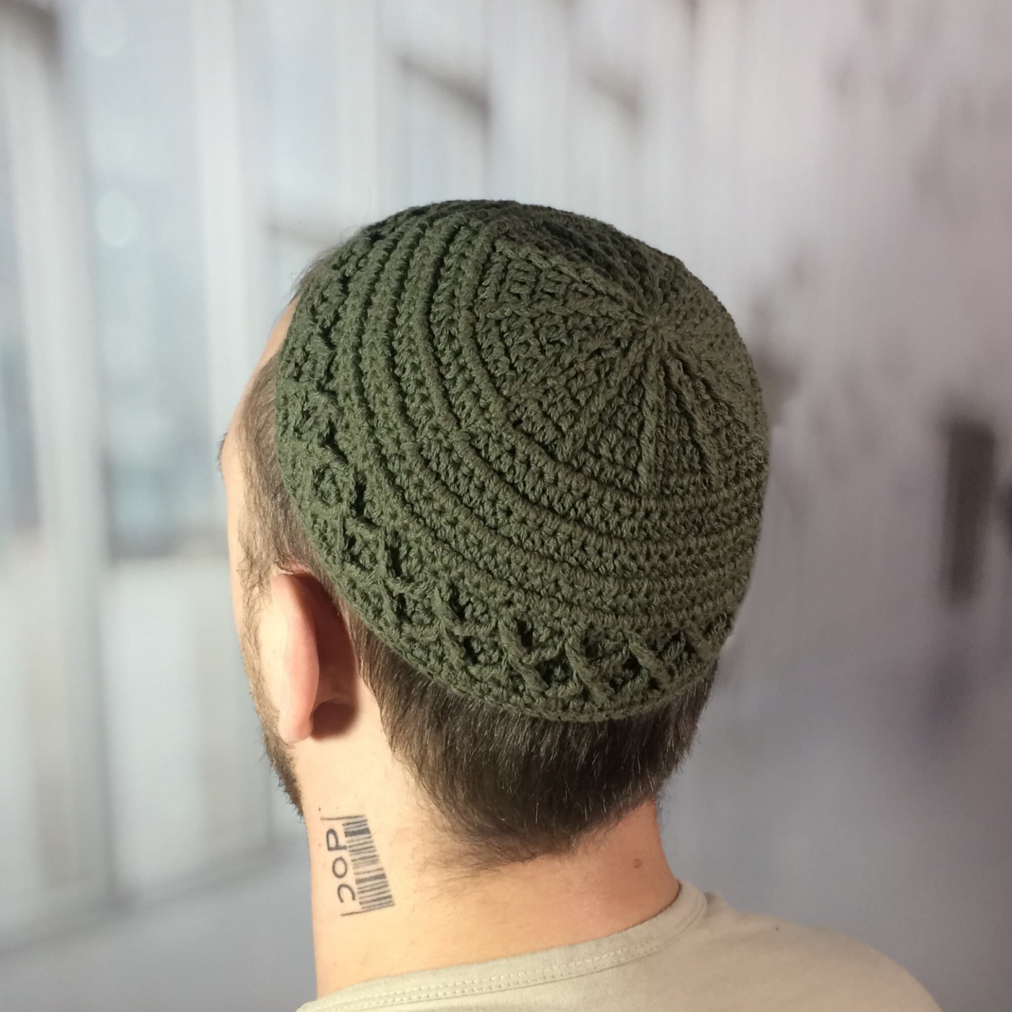 Olive green crocheted skull cap with a textured design. The cap features a circular pattern on top and a decorative border. This handmade headwear is suitable for various occasions.