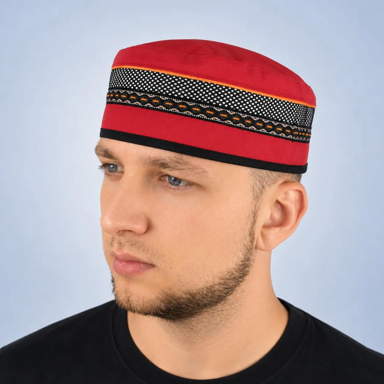 A man wearing a bright red linen Kufi hat with black trim, posing in a close-up side profile view against a neutral background.