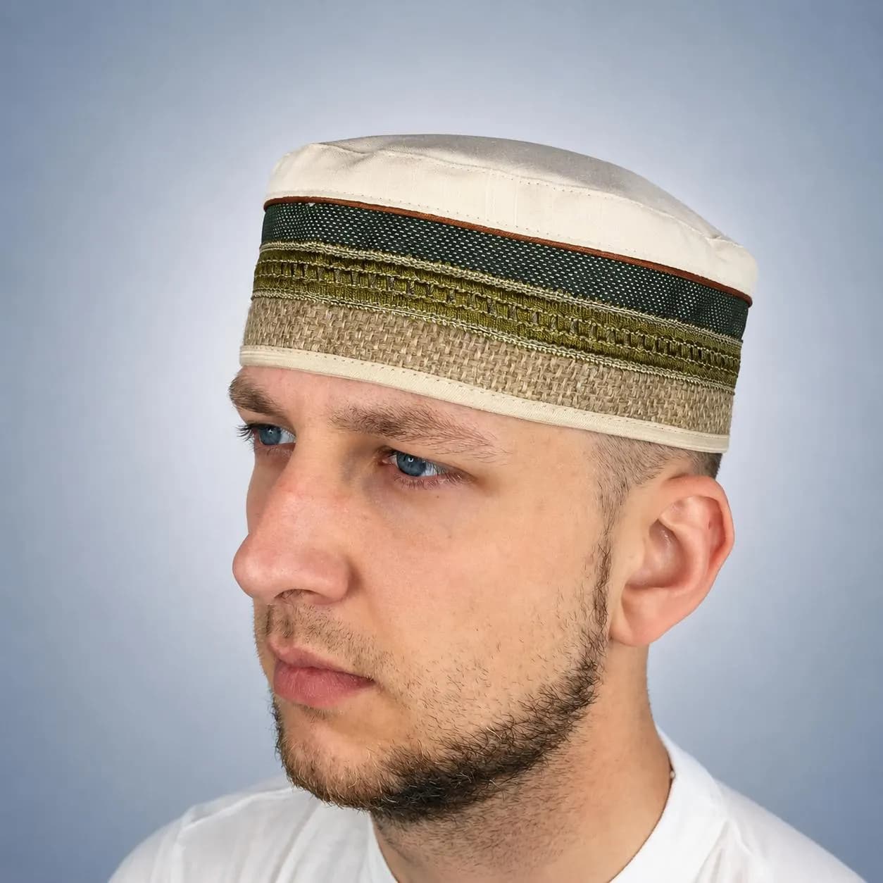 Close-up profile of a man wearing a white Islamic prayer hat with a wide dark green and gold embroidered border.