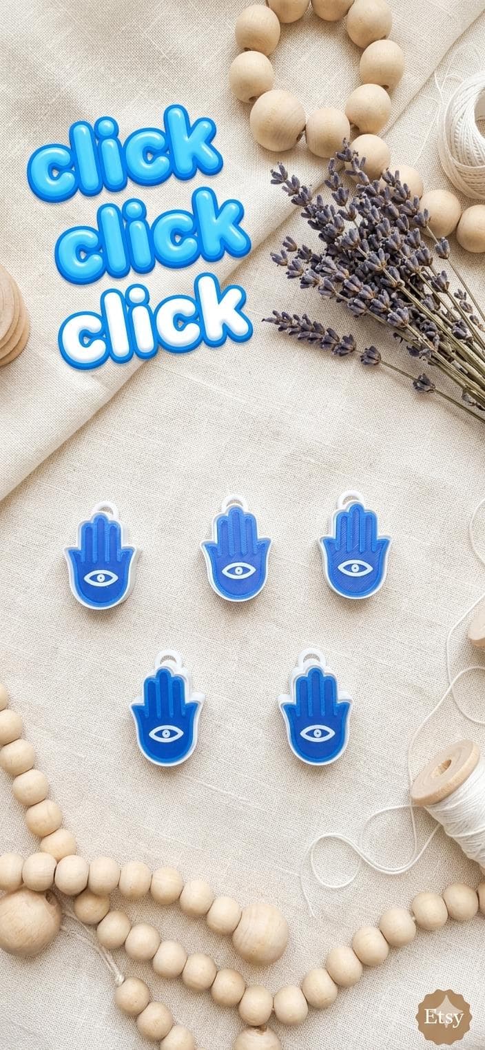 A blue Hamsa hand or hand of fatima charm with a central white eye icon featuring. The text CLICK CLICK CLICK is visible above the charm, accompanied by a starburst graphic.