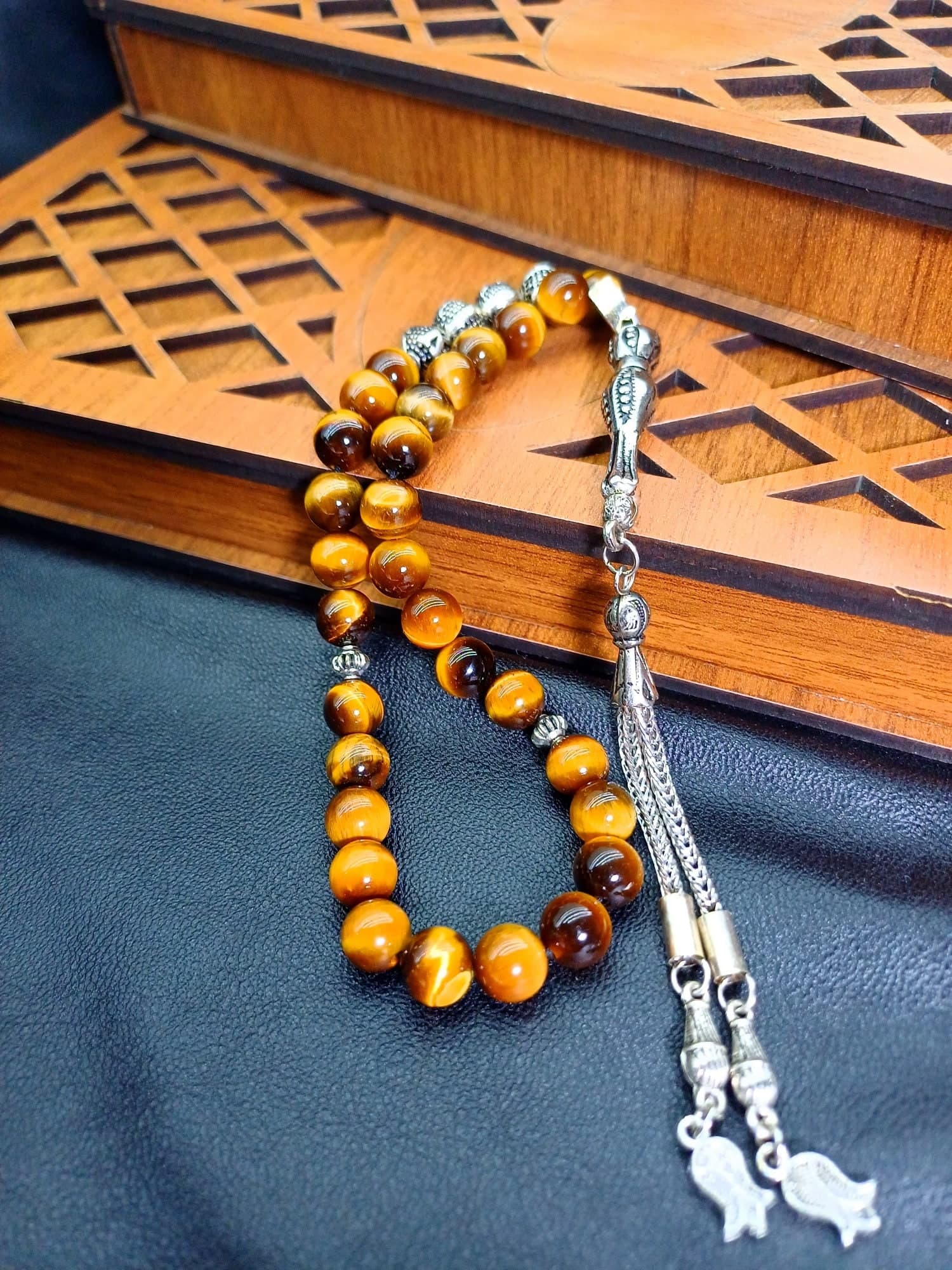 A brown and gold prayer beads with silver accents and tassels. The beads are made of tiger's eye stone.