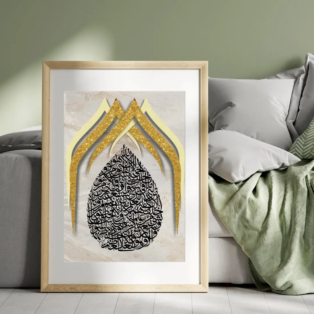 May include: Framed art print featuring Arabic calligraphy in black, set against a marble-effect background. The artwork includes gold glitter accents and a light wooden frame. The print is displayed on a wall near a bed.