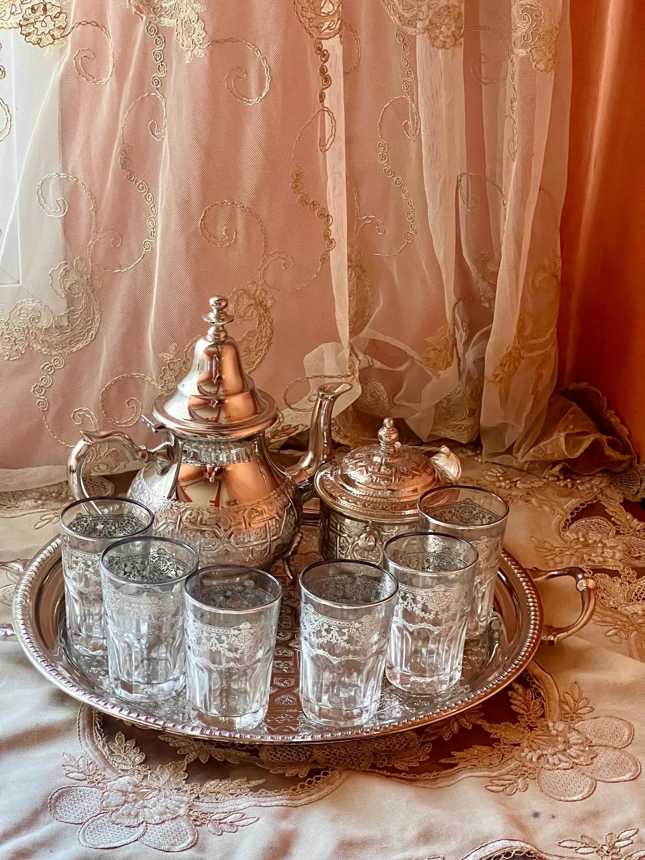 A front view of a silver Moroccan tea set with an ornate teapot, sugar bowl, and six glasses on a round tray.