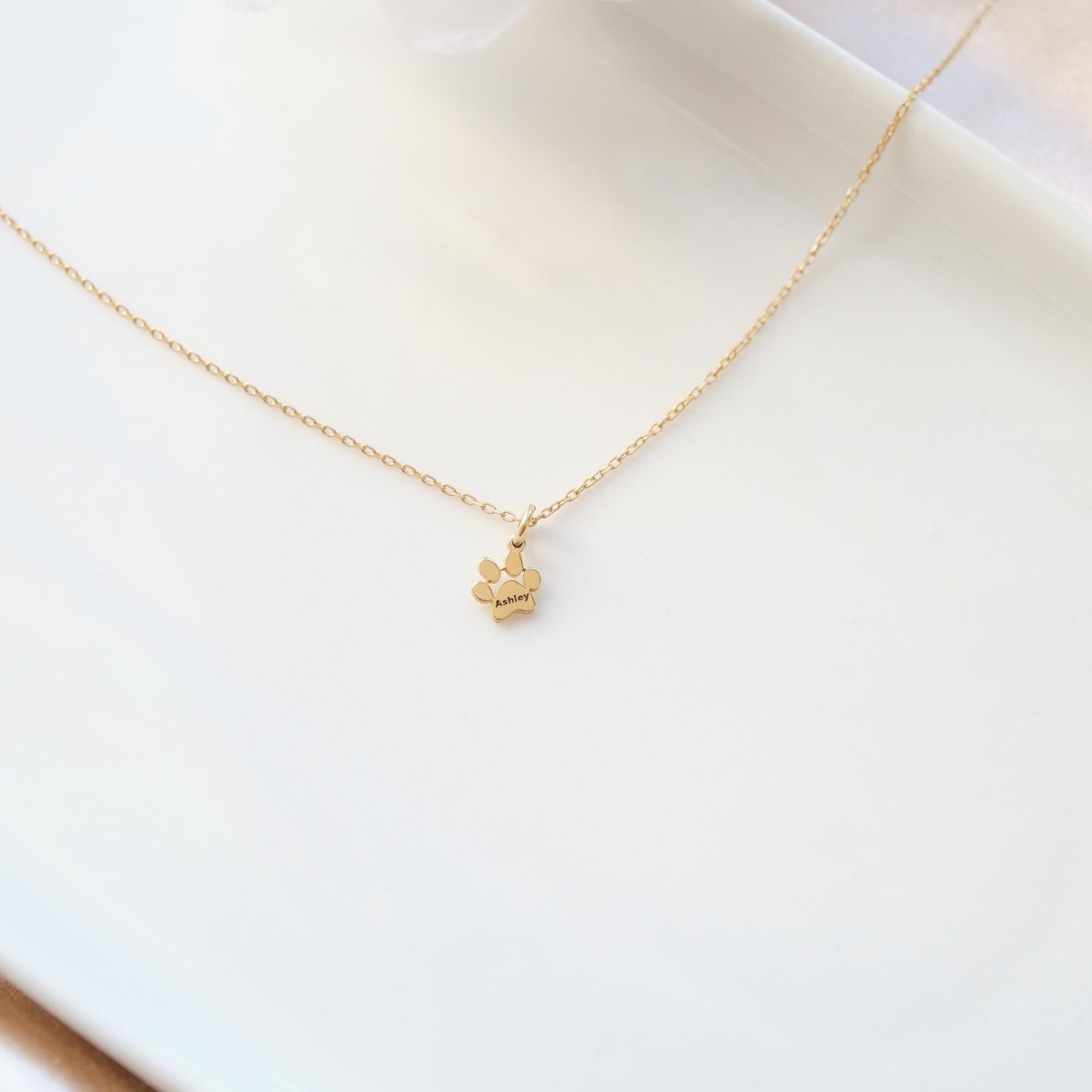 Close-up of custom gold paw print necklace with engraved pet name, dainty solid gold charm.