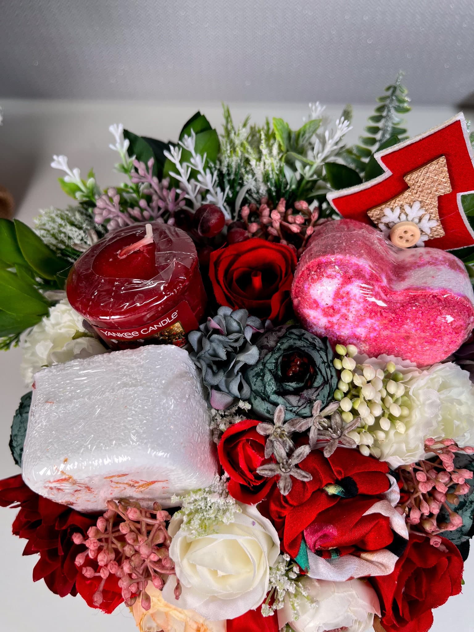 Red mistletoe box filled with artificial flowers and pamper products - bath bomb, shower steamer, yankee candle, satin headband