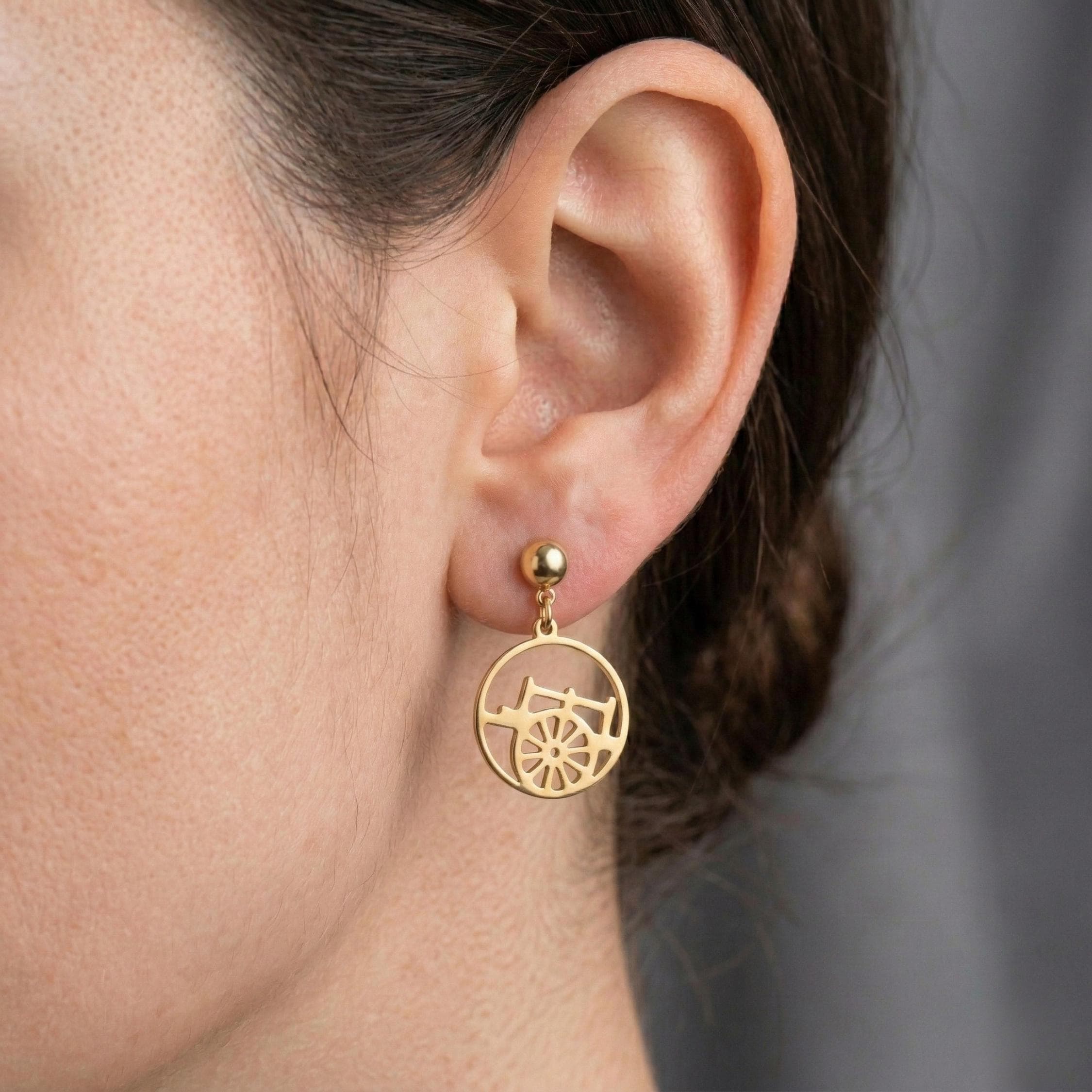 Sicilian wagon wheel Carretto siciliana stud earring in gold plated stainless steel worn by a model.