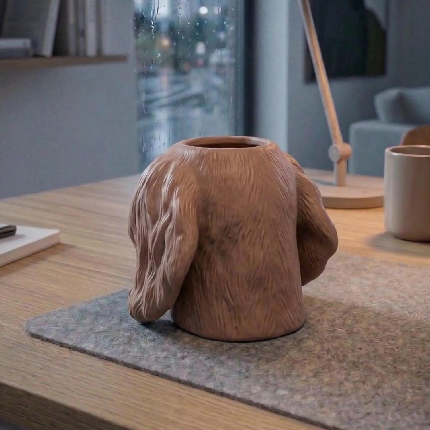 A brown 3D Printed vase with a unique design, resembling the back of a dog. The vase has a textured, fur-like appearance and a circular opening at the top. It sits on a gray felt mat on a wooden table.