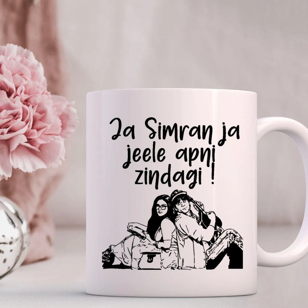 A white mug with a black and white illustration of two people sitting together, along with the text "Ja Simran ja jele ani zindagi!"
