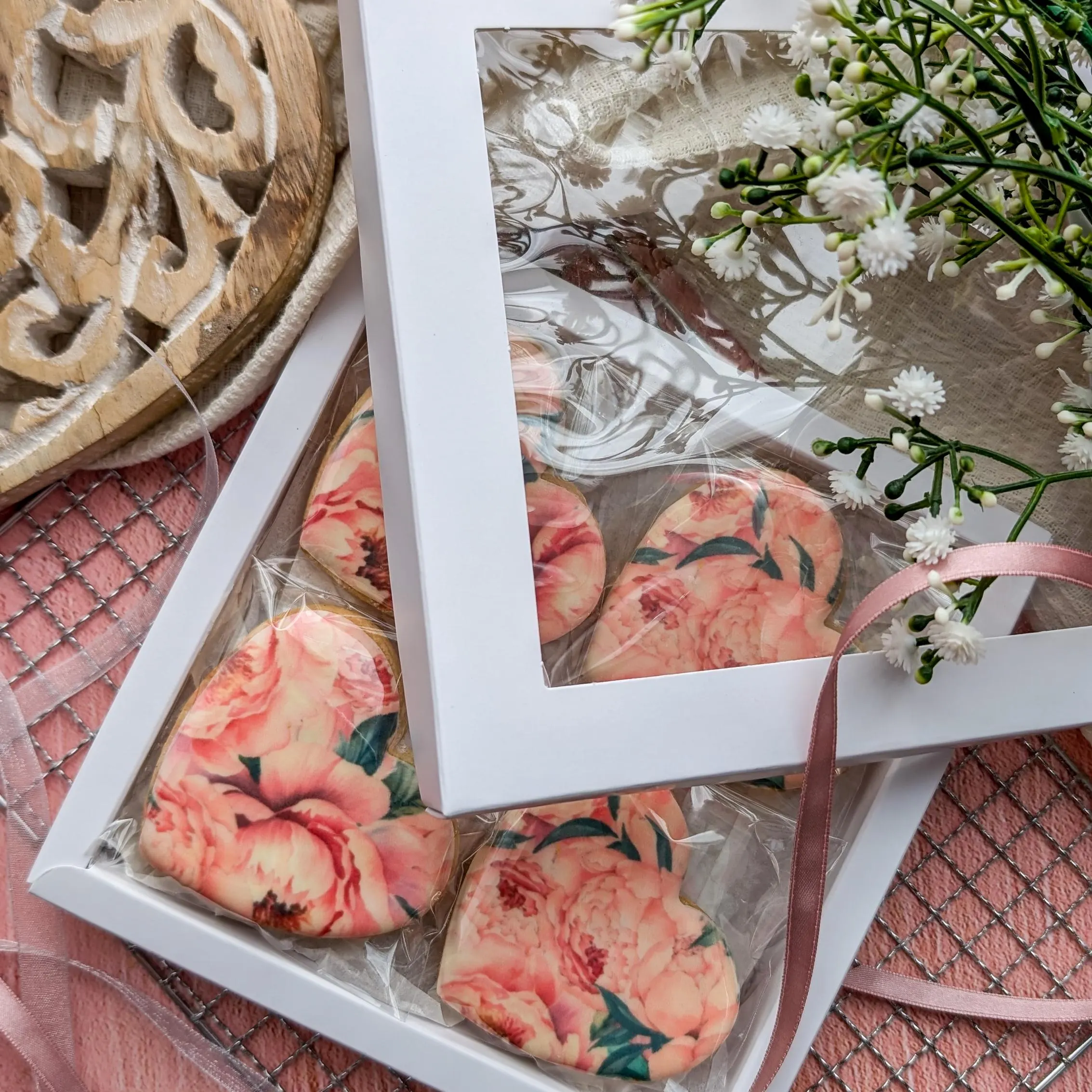Hand-Iced Biscuits Gift Box. The picture shows 8 heart shaped hand-iced biscuits printed with a pink peonies pattern, in a white gift box.
