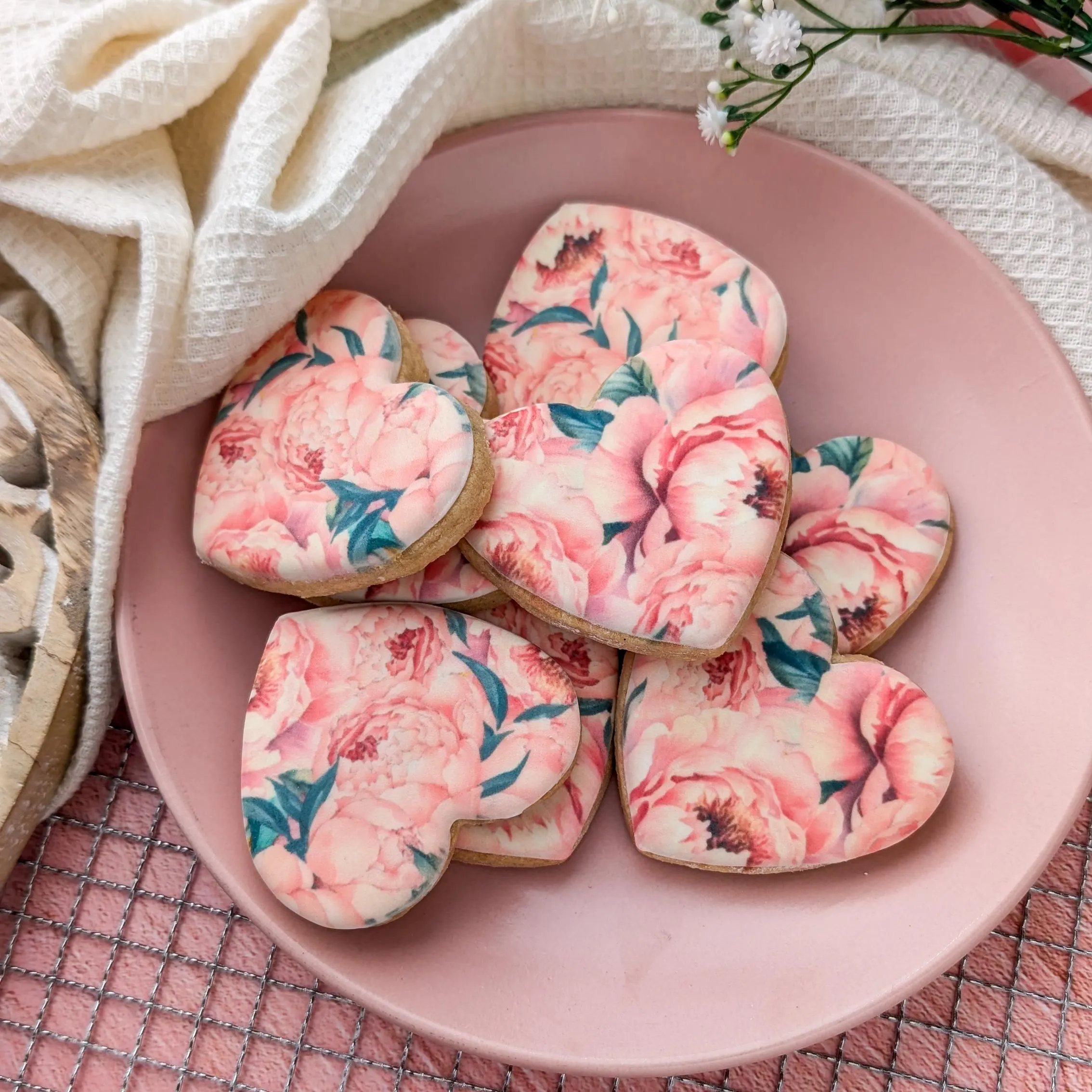 Hand-Iced Biscuits Gift Box. The picture shows 8 heart shaped hand-iced biscuits printed with a pink peonies pattern, served on a plate.