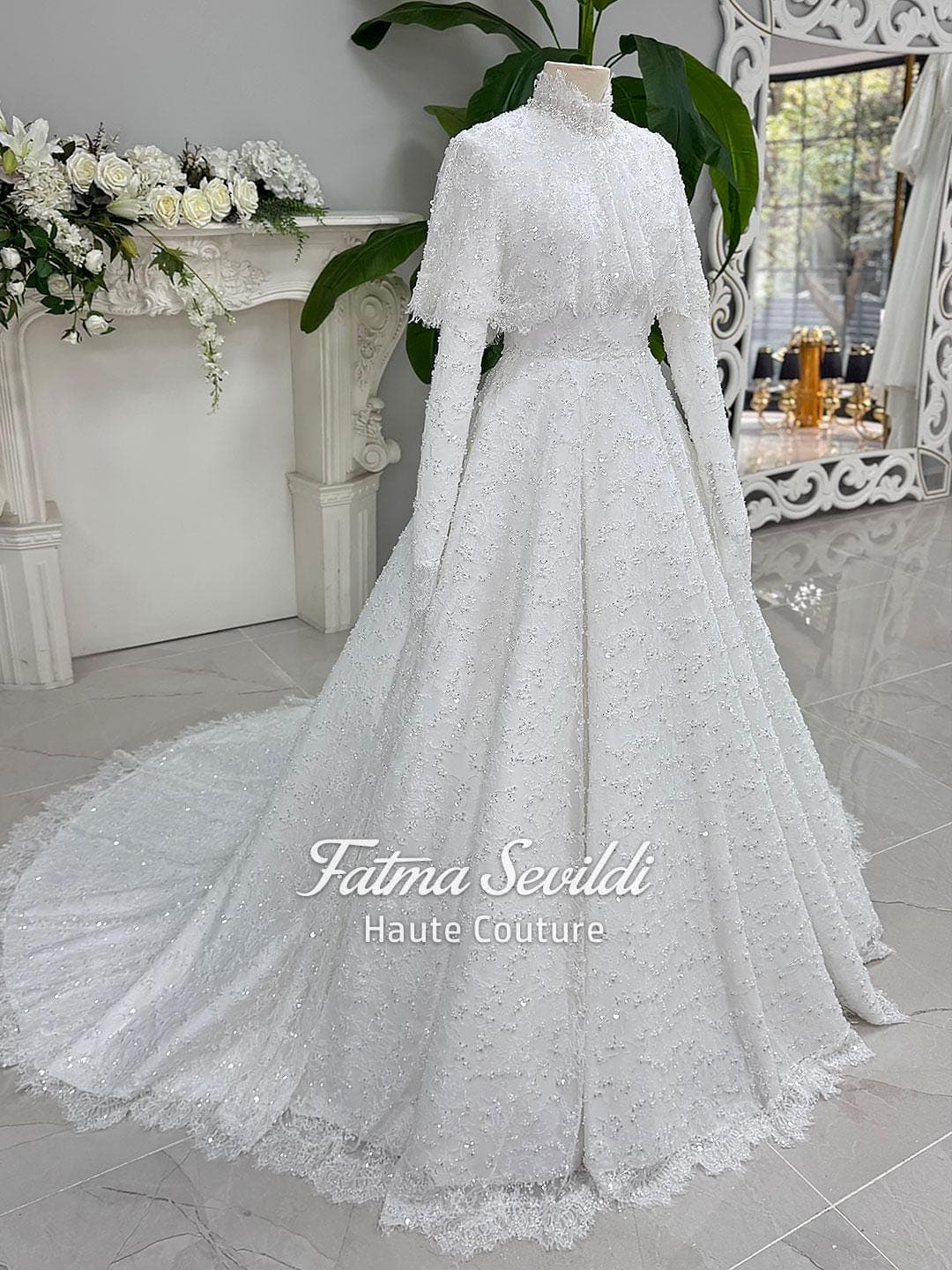 Veiled hijab wedding dress with high neck, long sleeves, and shimmering beaded lace in an elegant A-line silhouette. Includes premium lace veil, headscarf, and a lace short cape for a complete modest bridal set.