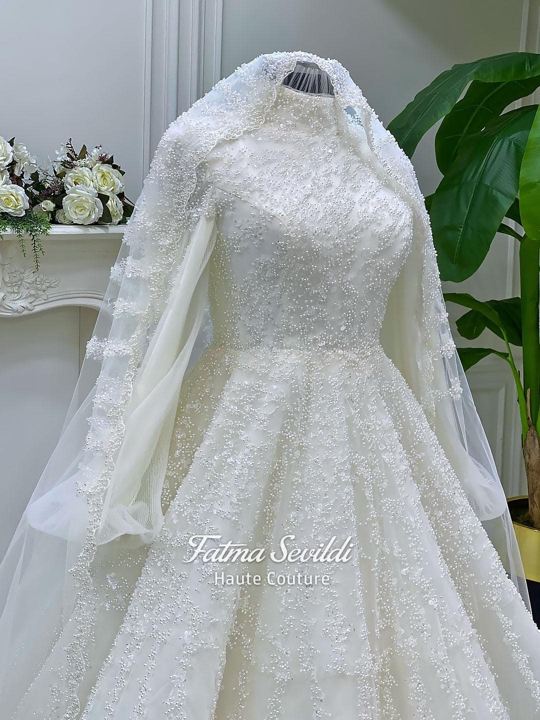 Luxury hijab wedding dress in an A-line tulle ball gown silhouette with long balloon sleeves, high neck, sparkling beadwork, and a lace-edged veil.