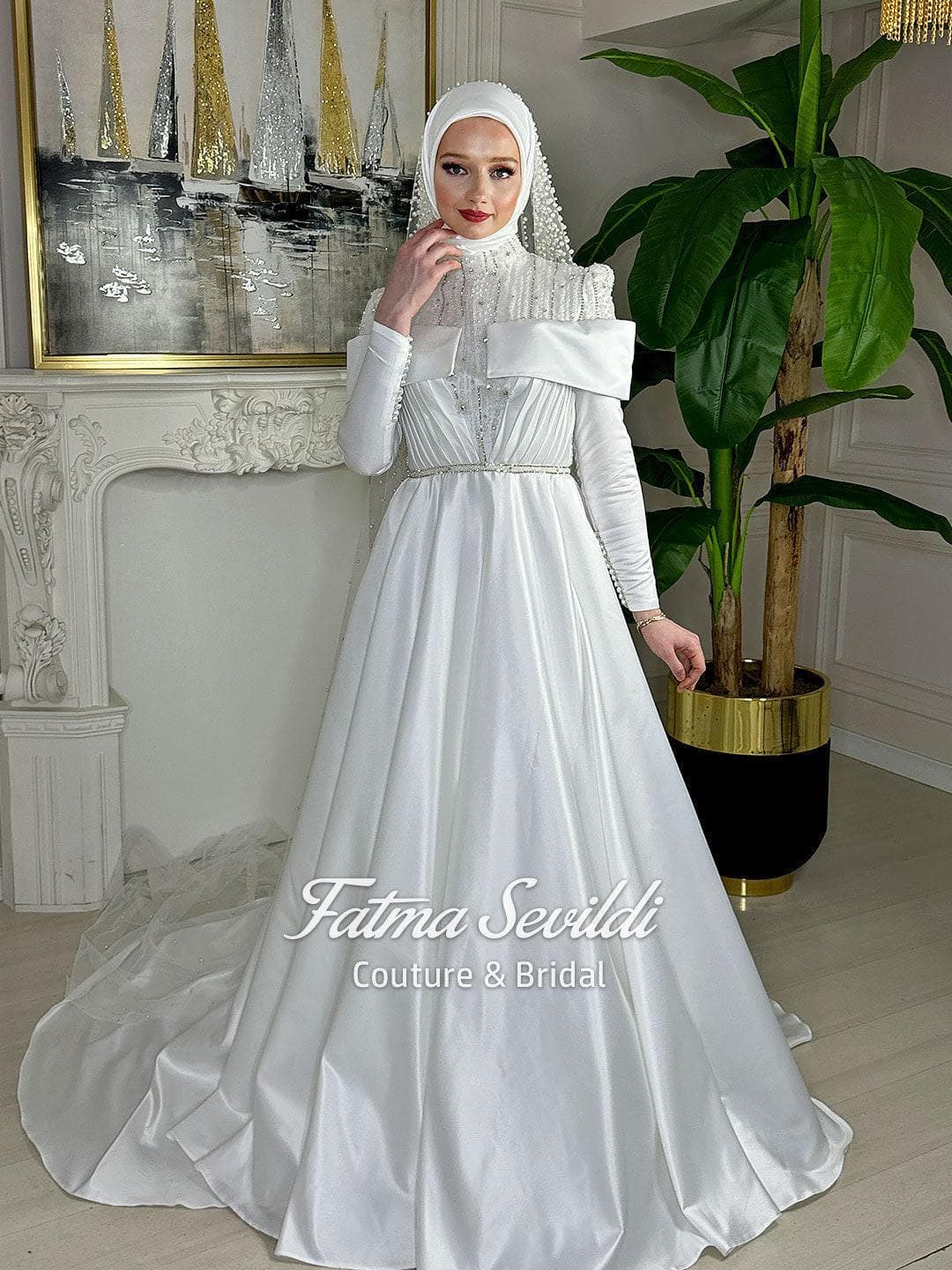 Luxury hijab wedding dress in satin A-line silhouette with high neck, long sleeves, and pearl-beaded tulle veil styling for a modest couture bridal look. Crafted for elegant Muslim and modest brides.