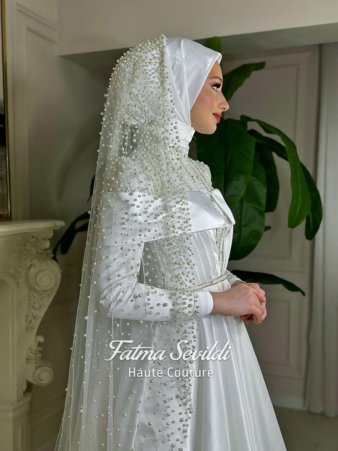 Luxury hijab wedding dress in satin A-line silhouette with high neck, long sleeves, and pearl-beaded tulle veil styling for a modest couture bridal look. Crafted for elegant Muslim and modest brides.