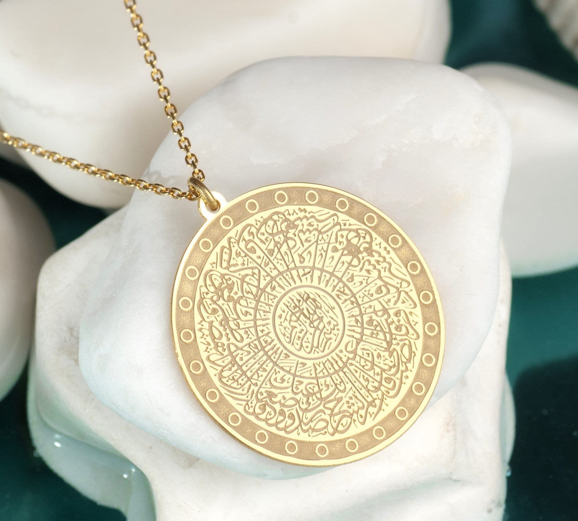 Surah Inshirah Necklace Necklace written  can be worn every day. It is made by hand in our workshop with care. All our jewelry is the most elegant choice for the bridesmaids, friends, your loved ones and for yourself. It is also a fact that silver jewelry improves blood circulation and provides electricity and makes you feel awake. A gold necklace with a round pendant featuring intricate Arabic calligraphy in a circular pattern. The pendant is surrounded by a decorative border of small circles.