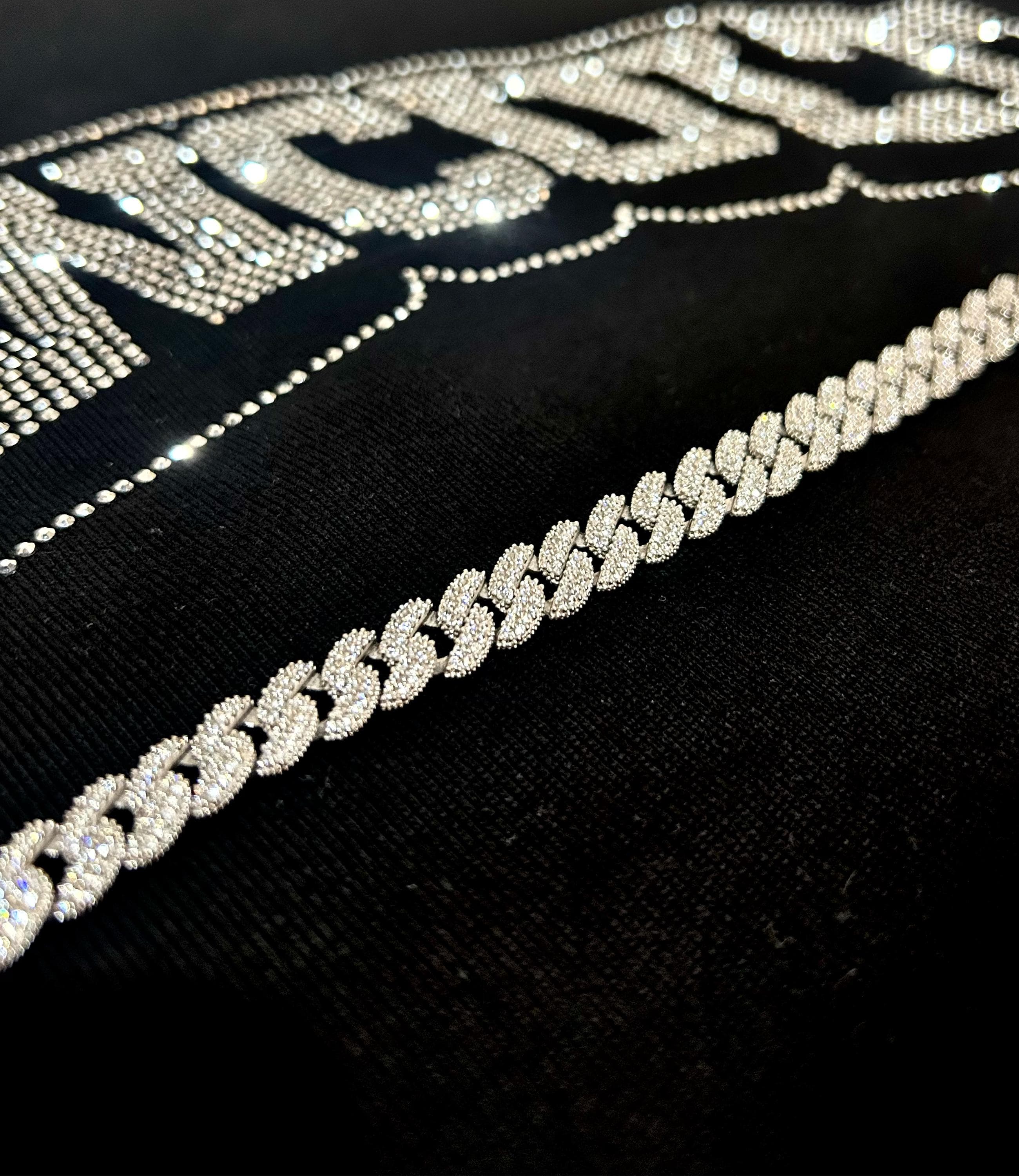 925 silver Cuban chain bracelet fully iced out with pavé stones, rhodium plated, photographed on concrete surface to reflect bold hip hop and streetwear aesthetic.