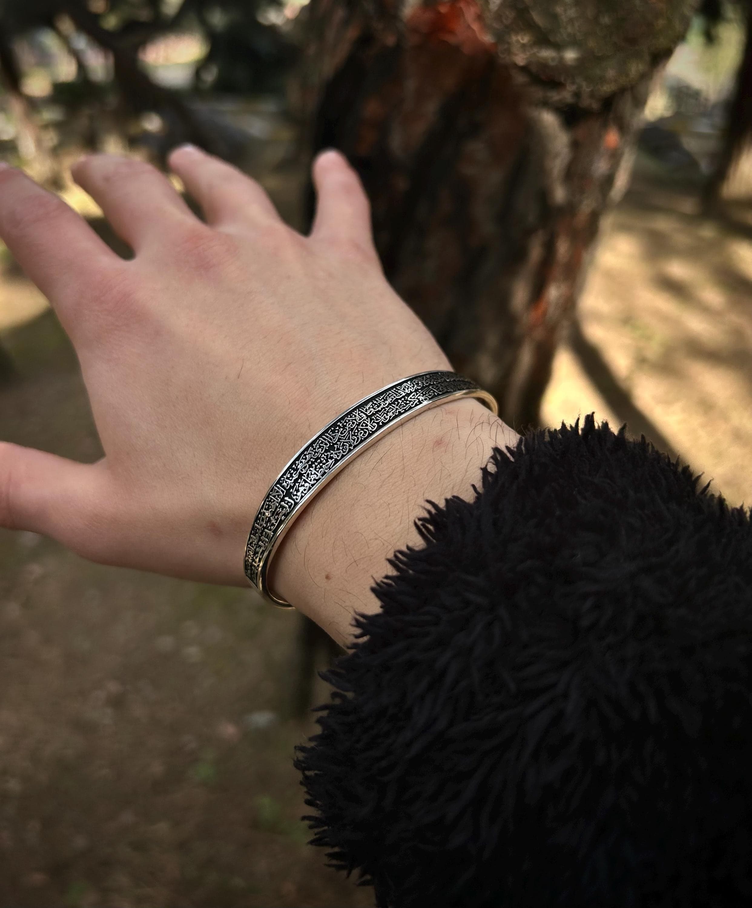 "A beautifully handcrafted 925 sterling silver cuff bracelet engraved with Ayat al-Kursi, photographed in natural light on a textured tree surface. This adjustable Islamic bangle is a meaningful spiritual jewelry piece, often worn for protection and blessings."