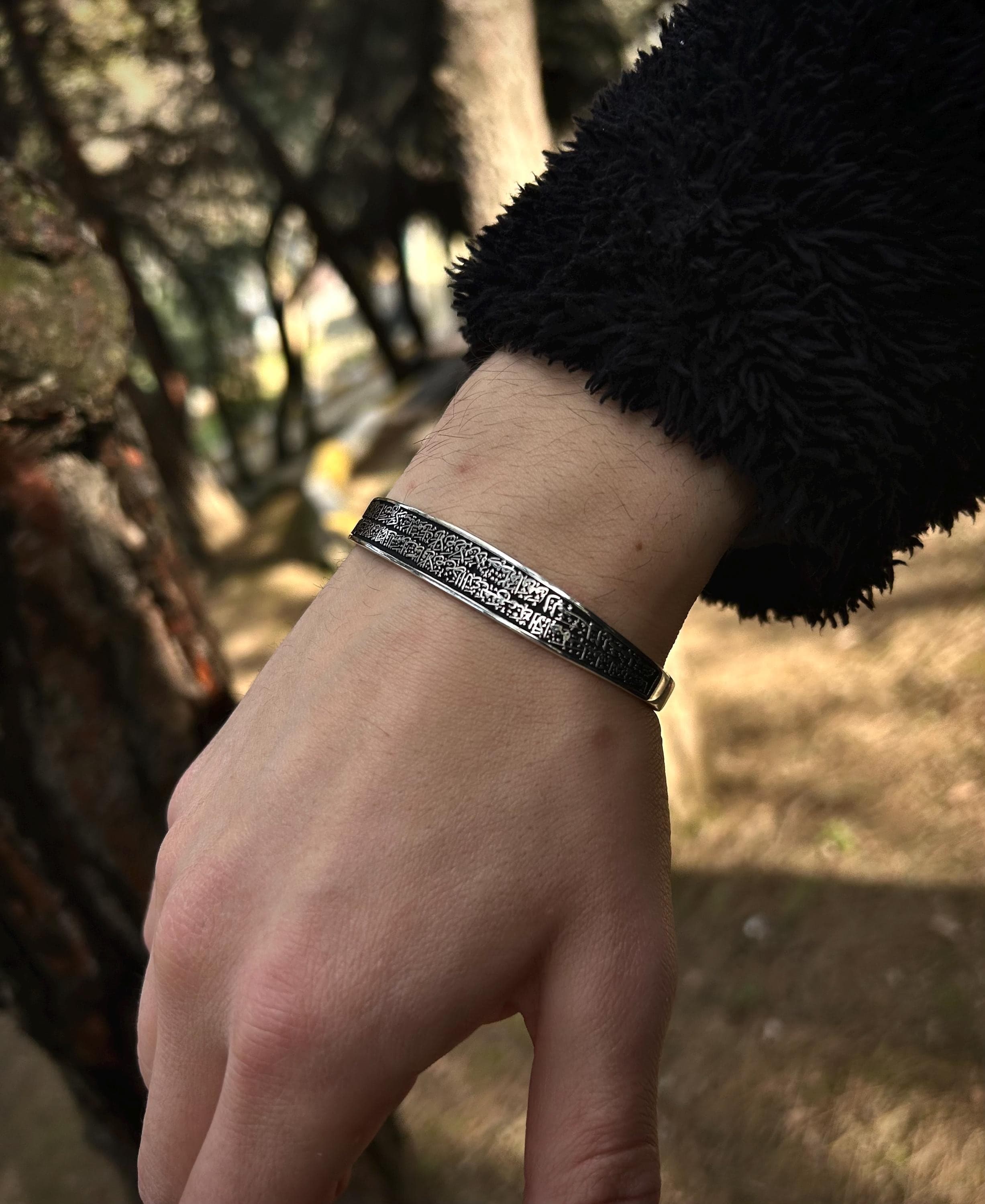 "A beautifully handcrafted 925 sterling silver cuff bracelet engraved with Ayat al-Kursi, photographed in natural light on a textured tree surface. This adjustable Islamic bangle is a meaningful spiritual jewelry piece, often worn for protection and blessings."