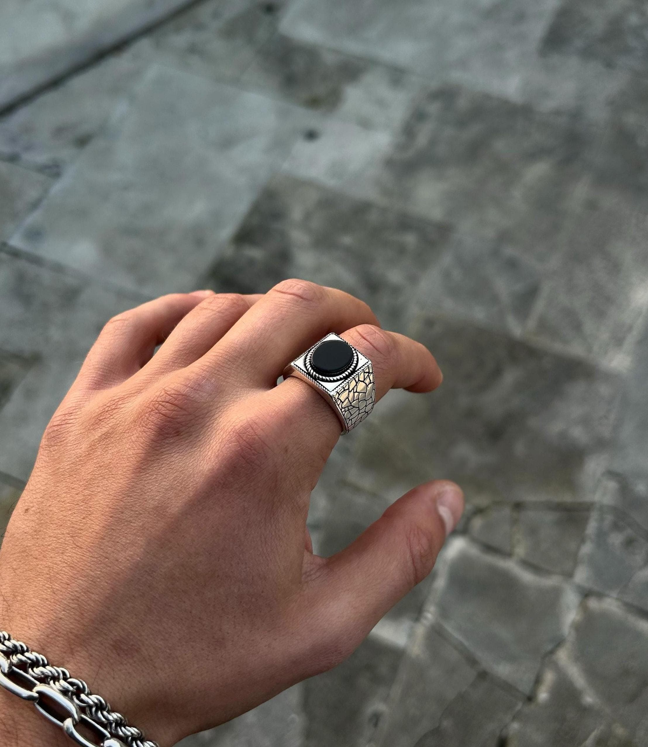 A men's 925 sterling silver statement ring featuring a round black onyx stone and a unique 'cracked earth' textured band, resting on dark, mossy tree bark to emphasize its grounding theme.