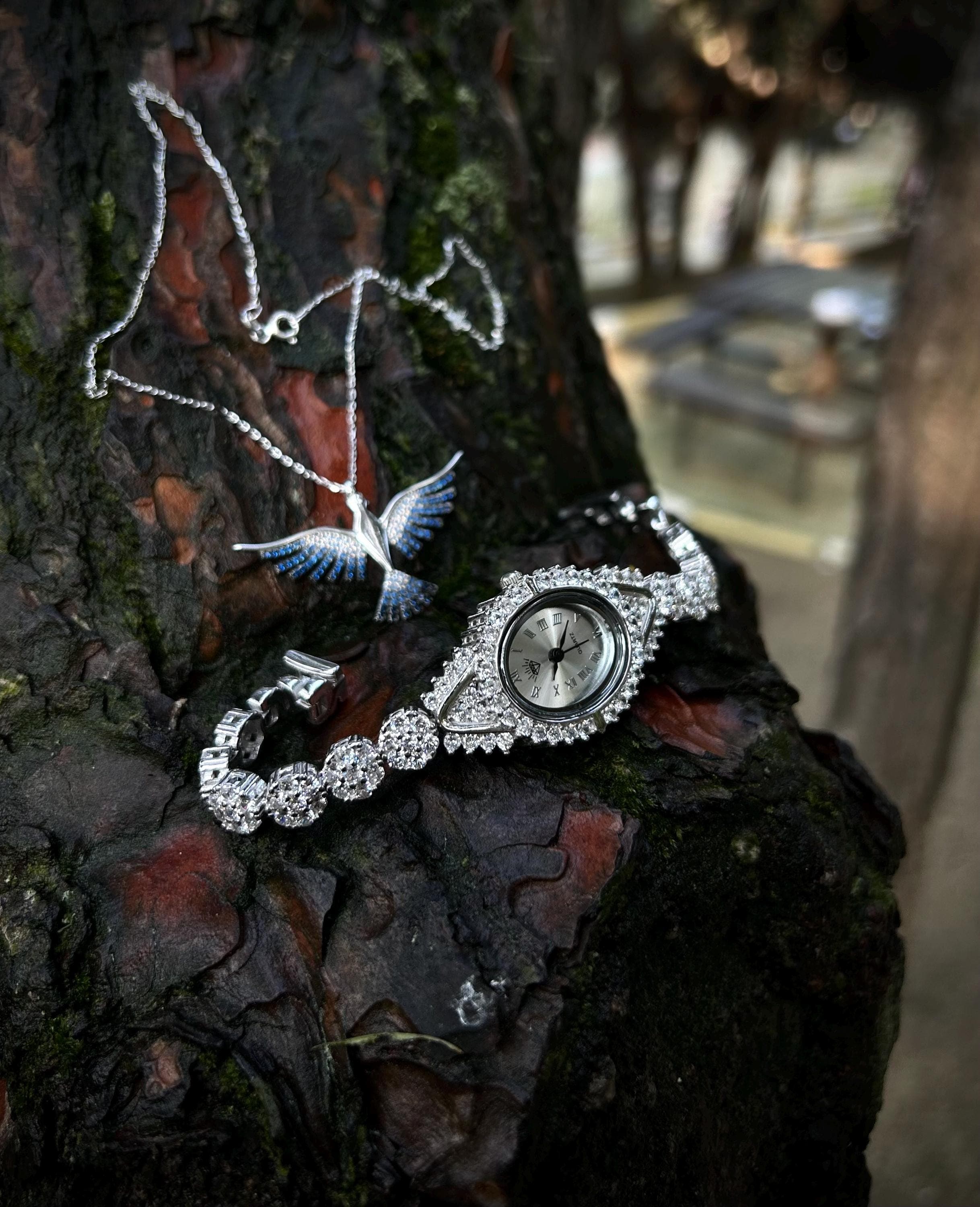Luxury 925 silver women's watch photographed in natural light, resting on a tree surface. Handmade with zircon stones and symbolic Phoenix necklace gift options.