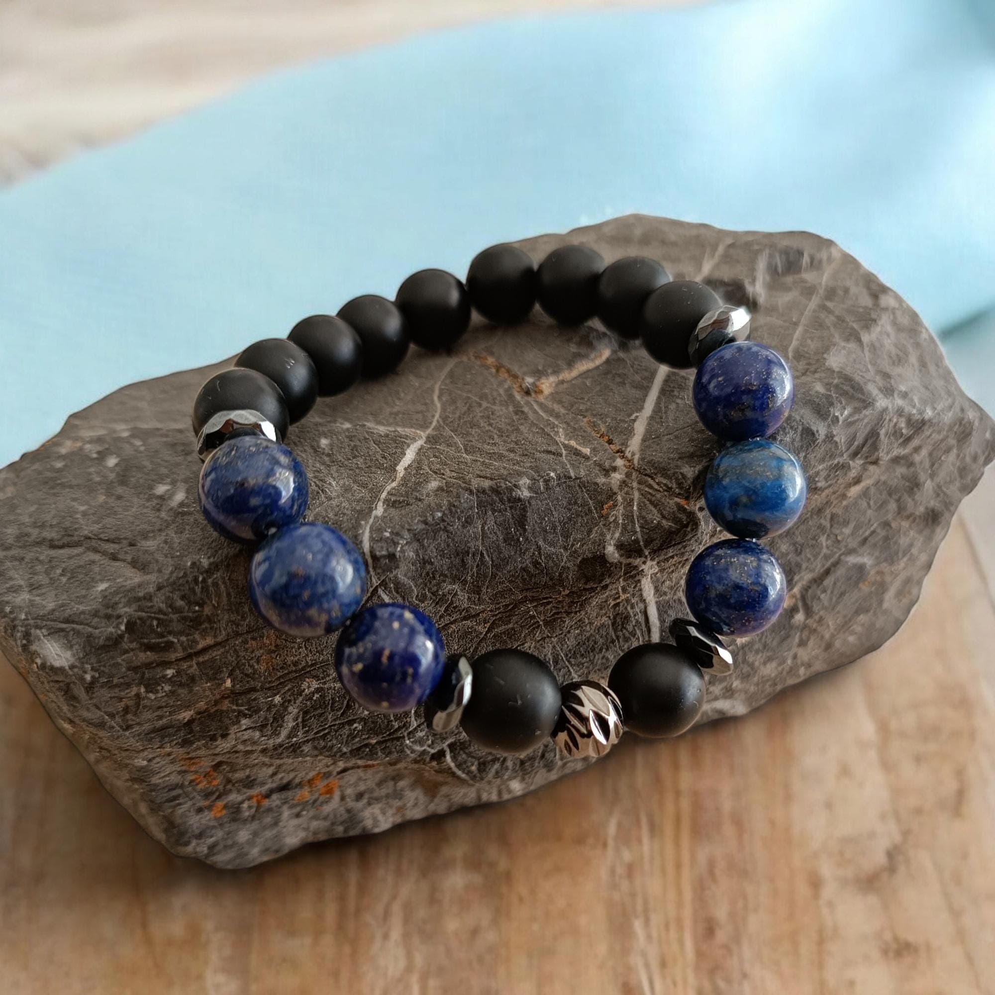 May include: A bracelet with black and blue beads. The bracelet is made of black onyx and lapis lazuli beads. The bracelet has a silver metal bead with a decorative design.