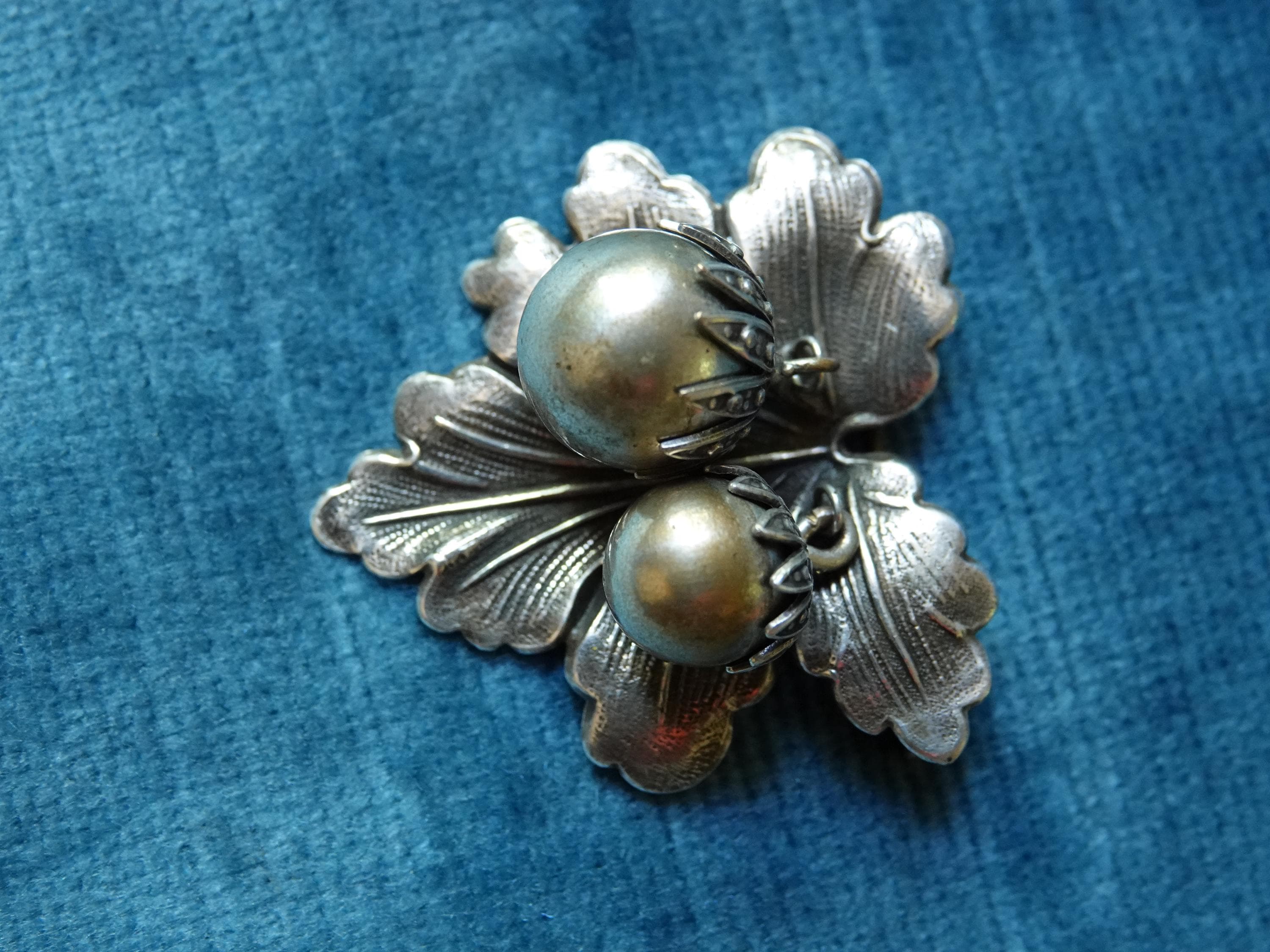 A silver brooch shaped like a leaf with two brass berry accents.