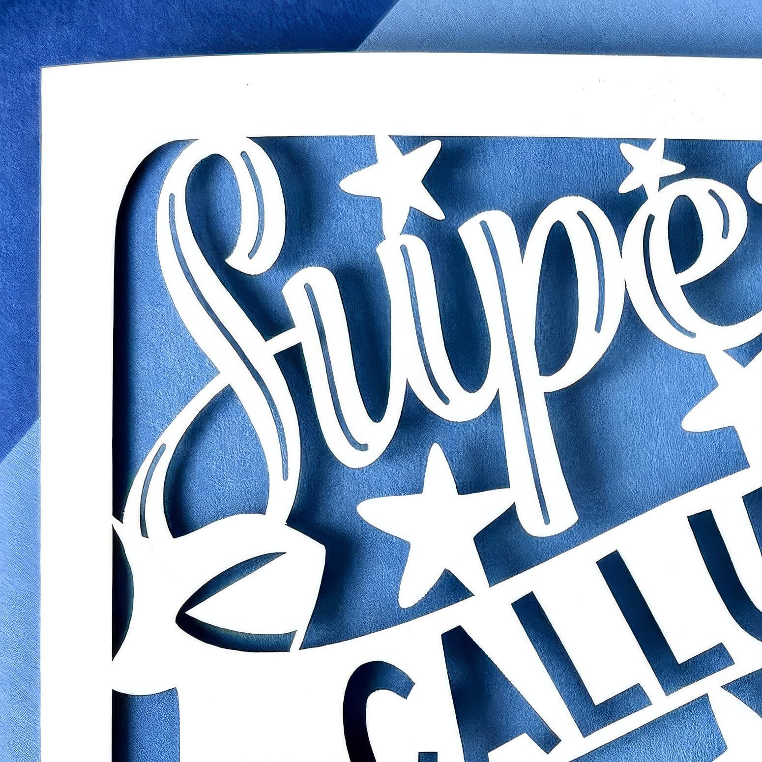 Close up of a white square laser cut Nephew birthday card. Featuring the words 'Super Nephew' in a bold script font across the top and bottom of the card, personalised with a name displayed on a banner in the centre. Hand‑drawn stars surround the design. The card has a pale blue paper insert.