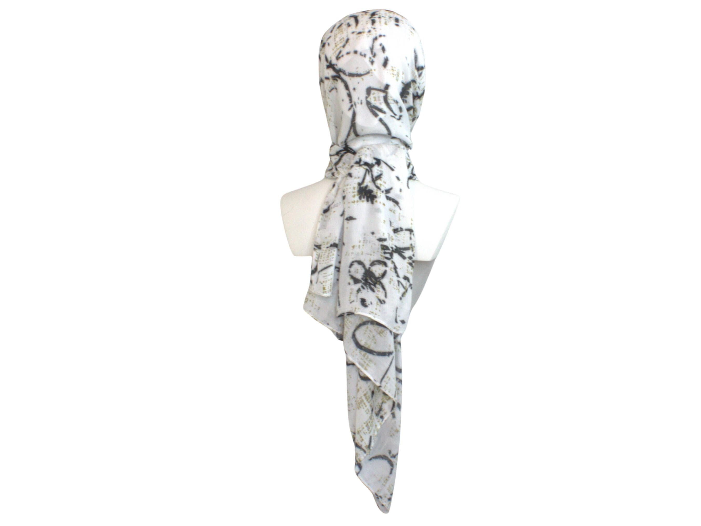 A printed bamboo modal white head scarf with a black and gold abstract print. The scarf is draped over a mannequin's head and shoulders.