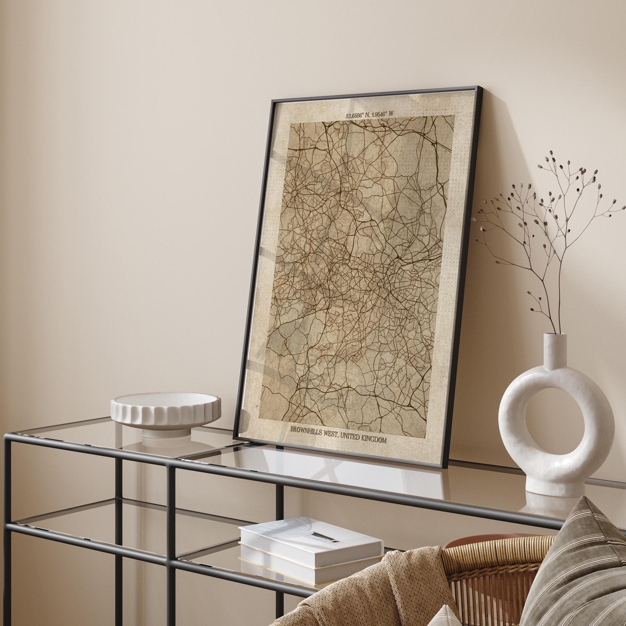 a framed map of the Brown's West region, which is a part of the United Kingdom, displayed on a glass table. The table also has a white vase and a book on it.