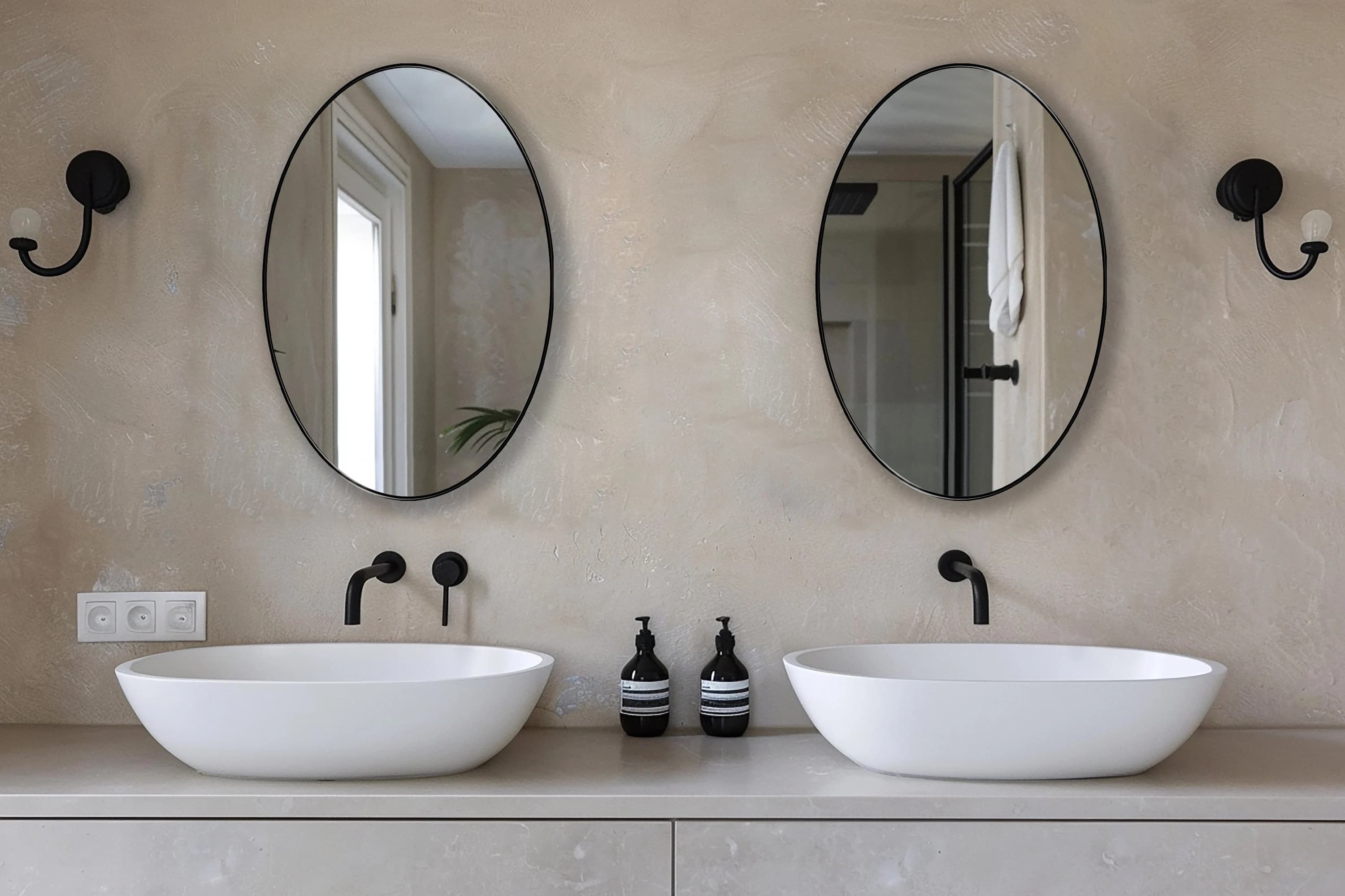 Two Oval Mirror with black frame finish hang on the wall of a powder room over a double vanity.
