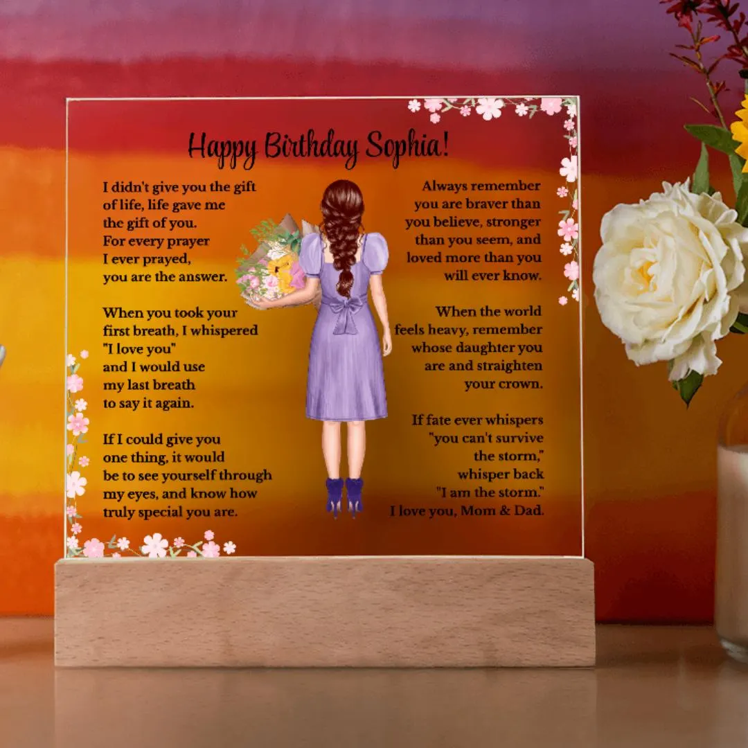 May include: A personalized acrylic plaque displayed on a wooden LED base in a modern home setting. The custom design features a heartfelt birthday message, pink floral accents, and an illustrated girl with braided auburn hair wearing a purple dress and holding a bouquet. Decorative rose and multi-colored wall are shown in the background.