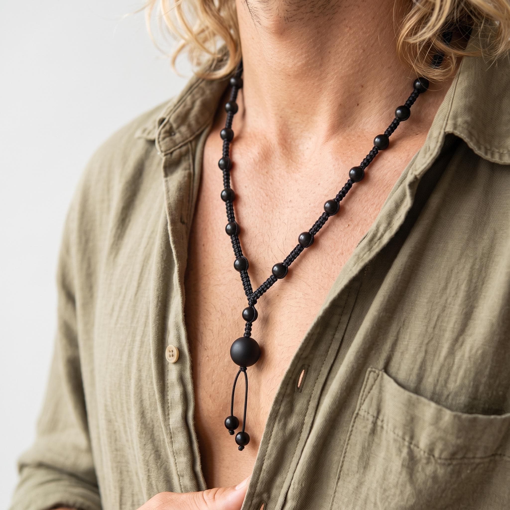 Natural black onyx gemstone rosary style necklace for men with a hand braided macrame cord laying flat on a textured slate surface.