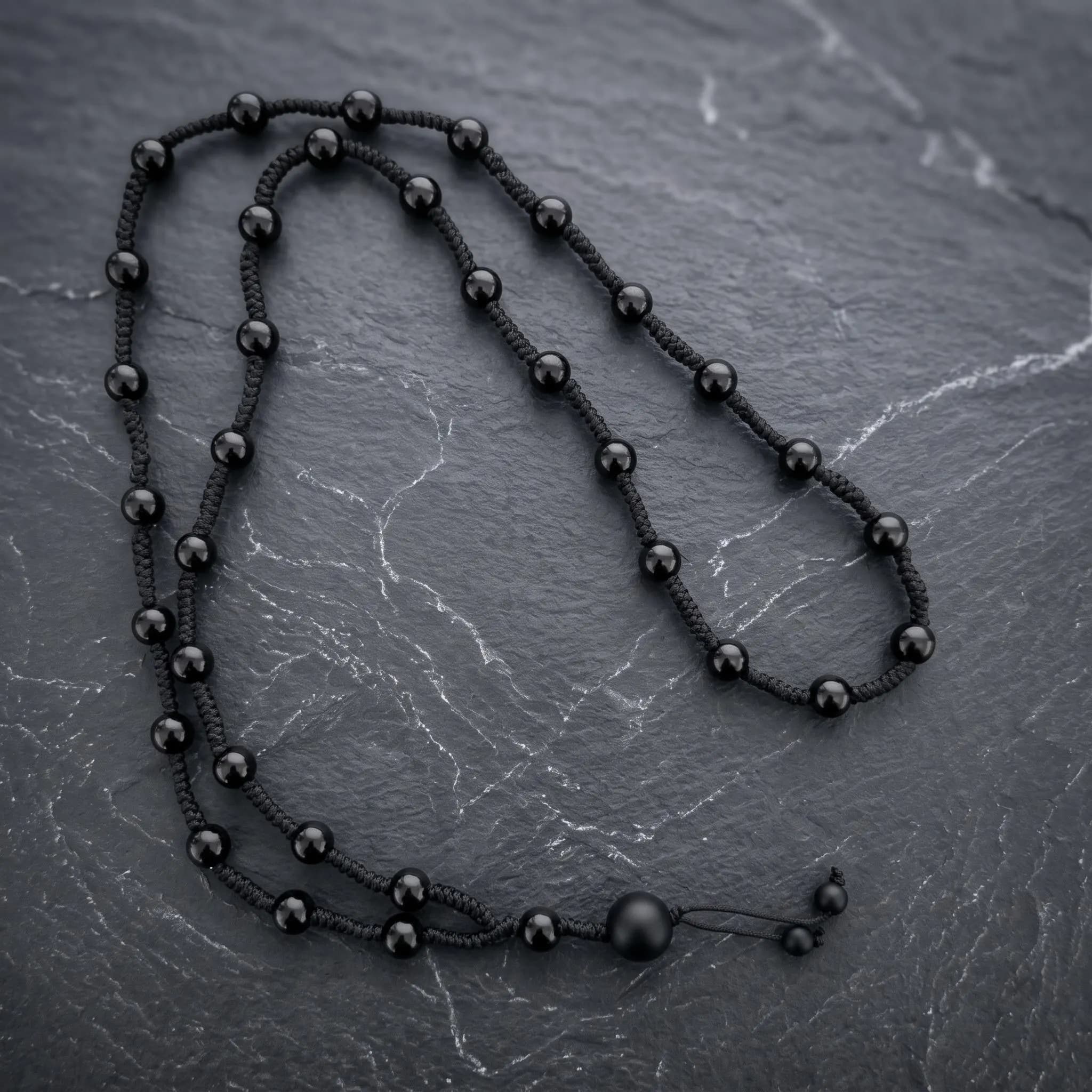 A bohemian style men's black onyx macrame necklace displayed on a dark stone surface showing the hand braided paracord craftsmanship.