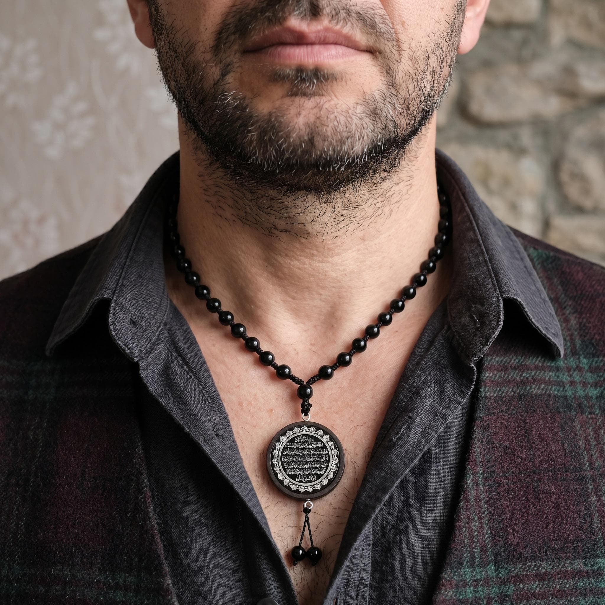 Close-up of a Muslim necklace for men showing the full Ayat al Kursi verse engraved on a black and silver pendant with macrame knotting.