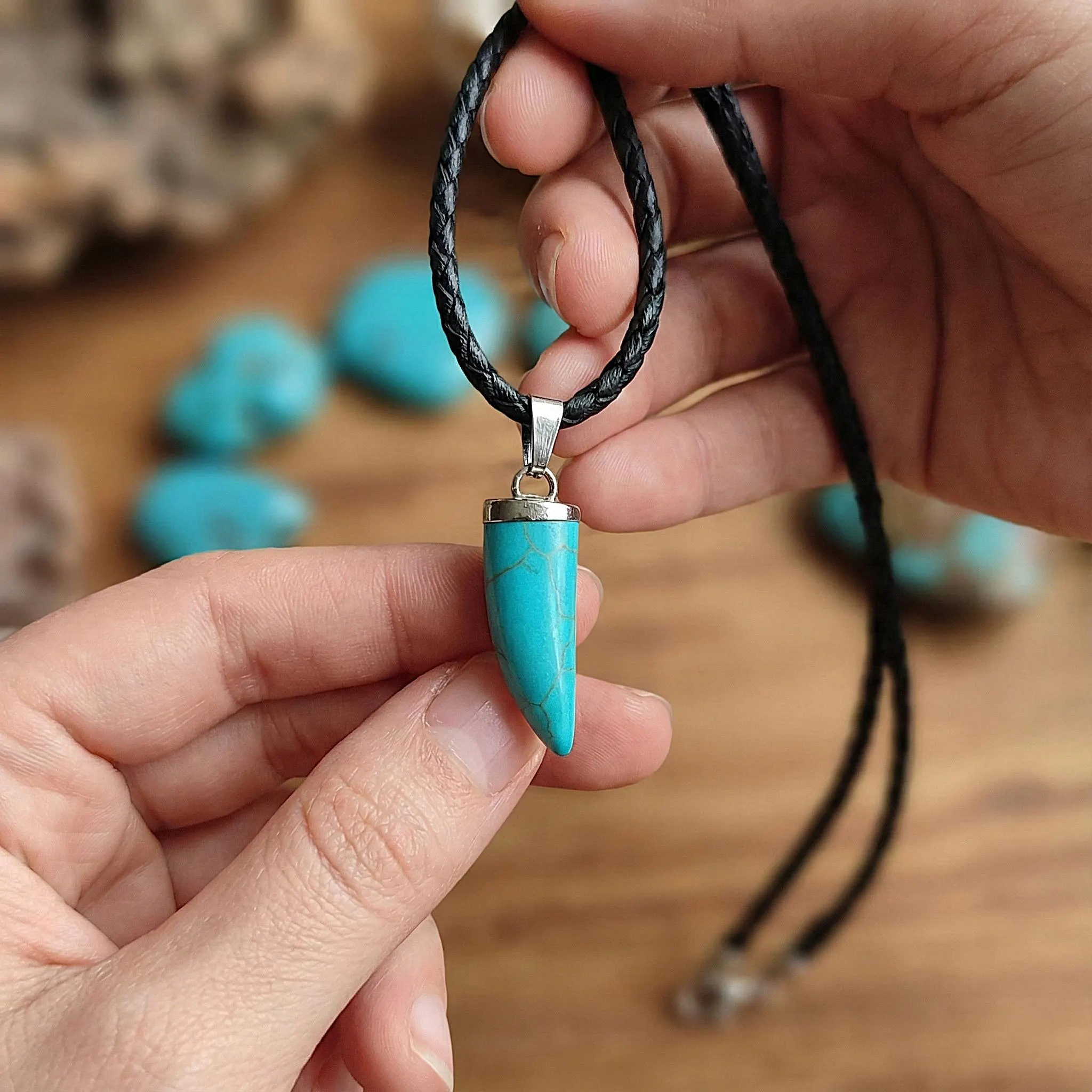 Close up of blue turquoise stone pendant resembling a wolf tooth or claw, rustic tribal jewelry design with durable leather strap for men.