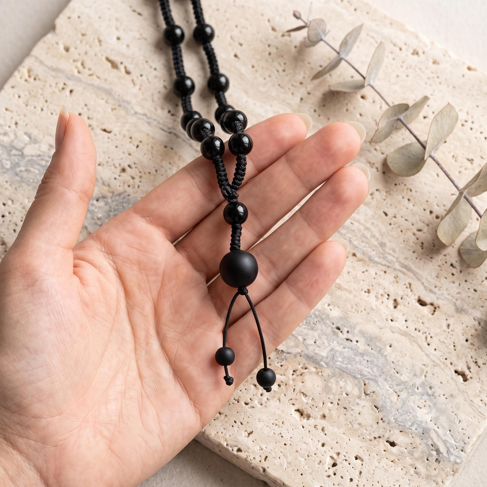 A male model wearing the hand knotted black onyx stone necklace with a relaxed bohemian khaki linen shirt against a clean background.