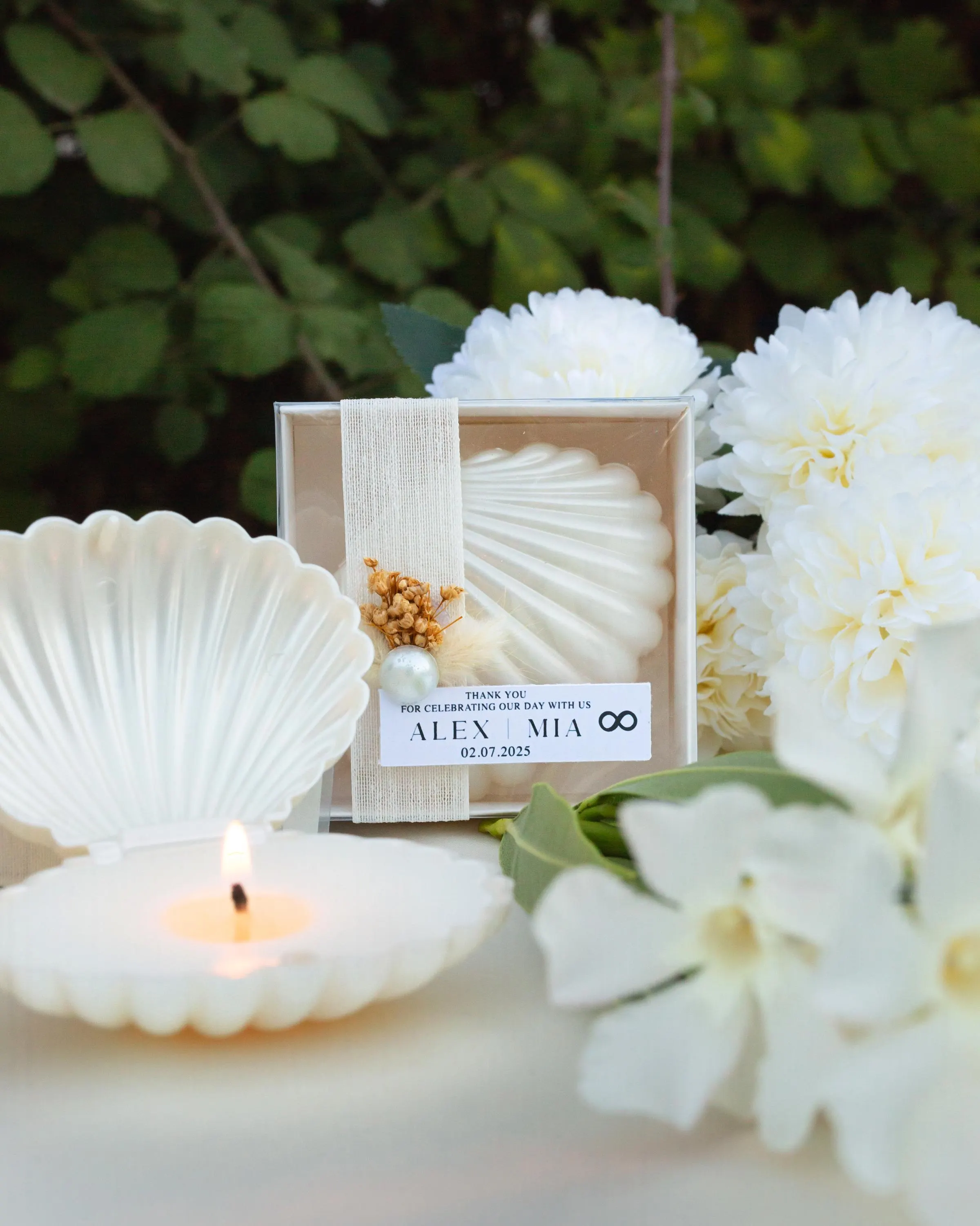 Handmade sea shell candle favor with ribbon and dried floral accents in a clear acetate box, personalized beach wedding guest gift.