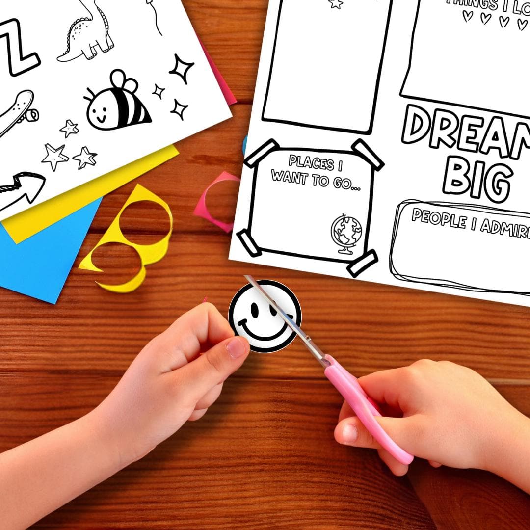 Child cutting out a smiley face from a printable Kids Vision Board 2026 craft sheet with scissors on a wooden table. Fun goal setting activity and New Year project for children featuring coloring pages, kid affirmations, and Dream Big vision board templates for creative goal planning.