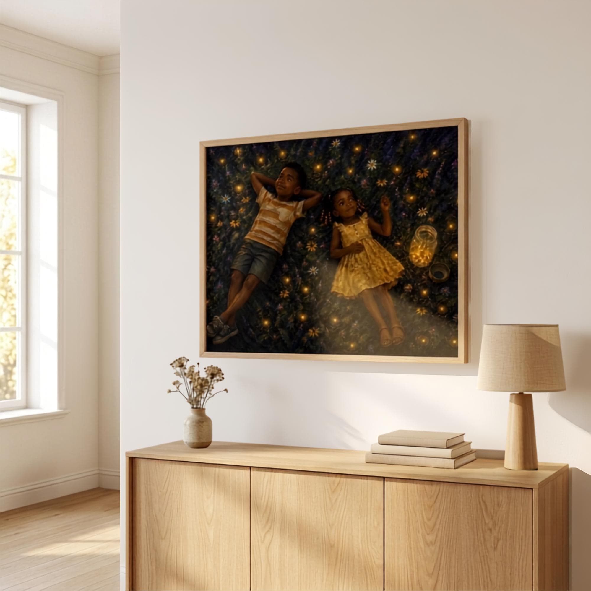 Horizontal Firefly Dreams wall art displayed above a natural oak sideboard in a warm modern living room, featuring two Black siblings lying beneath glowing fireflies on a magical summer night.