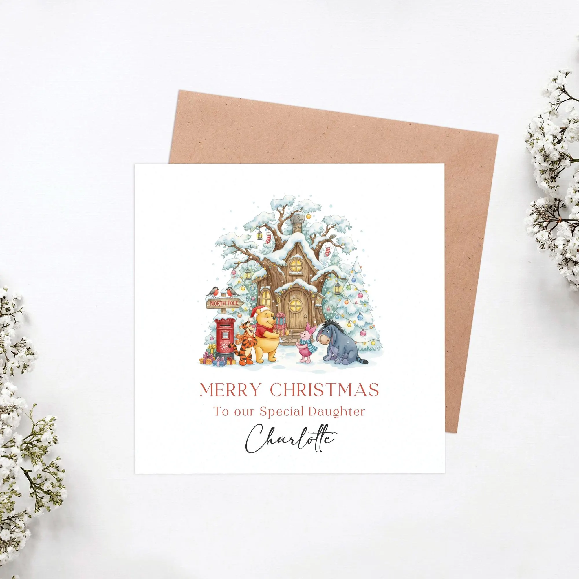 May include: A Christmas card with a festive illustration of Winnie the Pooh characters in a snowy setting. The card reads "Merry Christmas To our Special Daughter Charlotte". The card is square and set against a brown envelope.