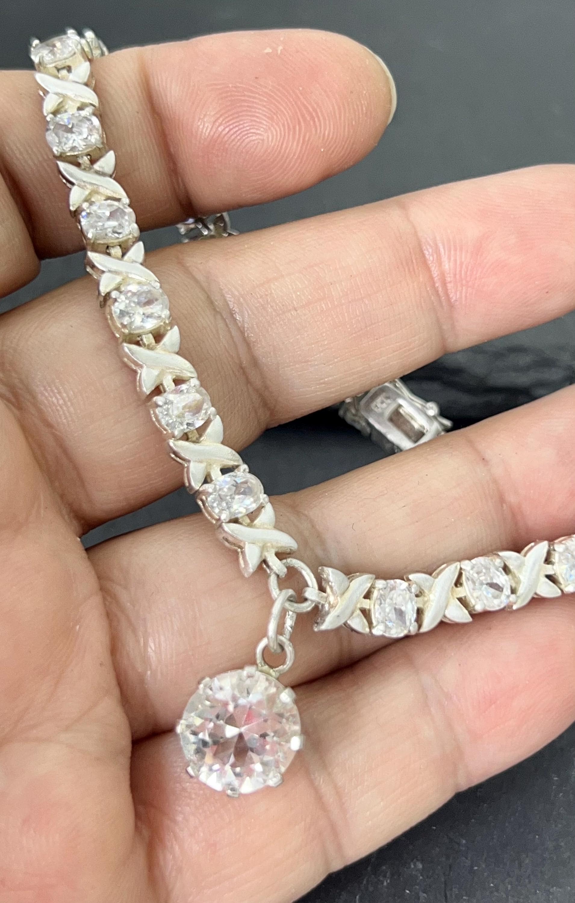 Product photo showing vintage 1980s XO bracelet in 925 sterling silver with cubic zirconia stones and drop charm, on a hand
