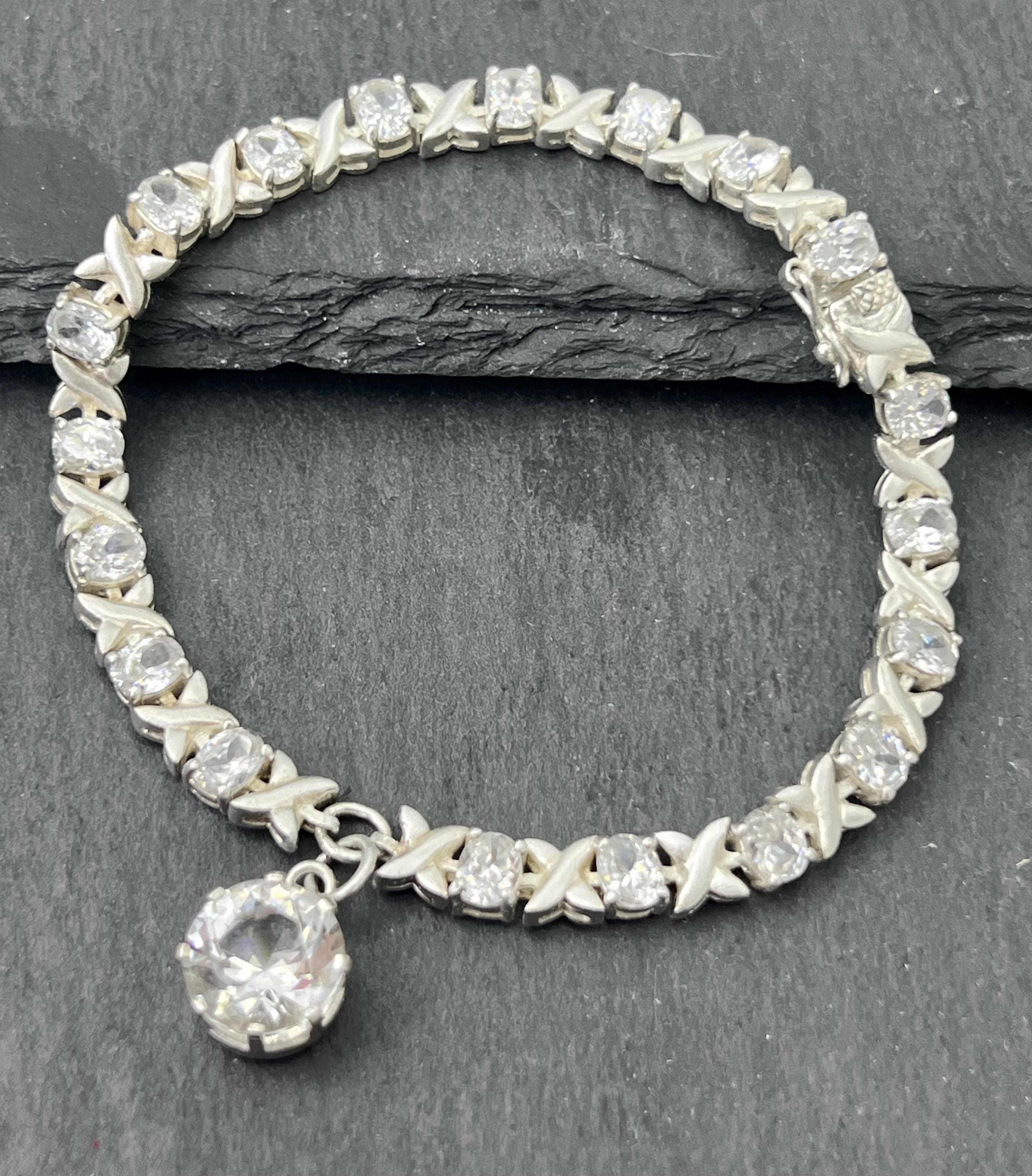 Product photo showing vintage 1980s XO bracelet in 925 sterling silver with cubic zirconia stones and drop charm, secured with box clasp.