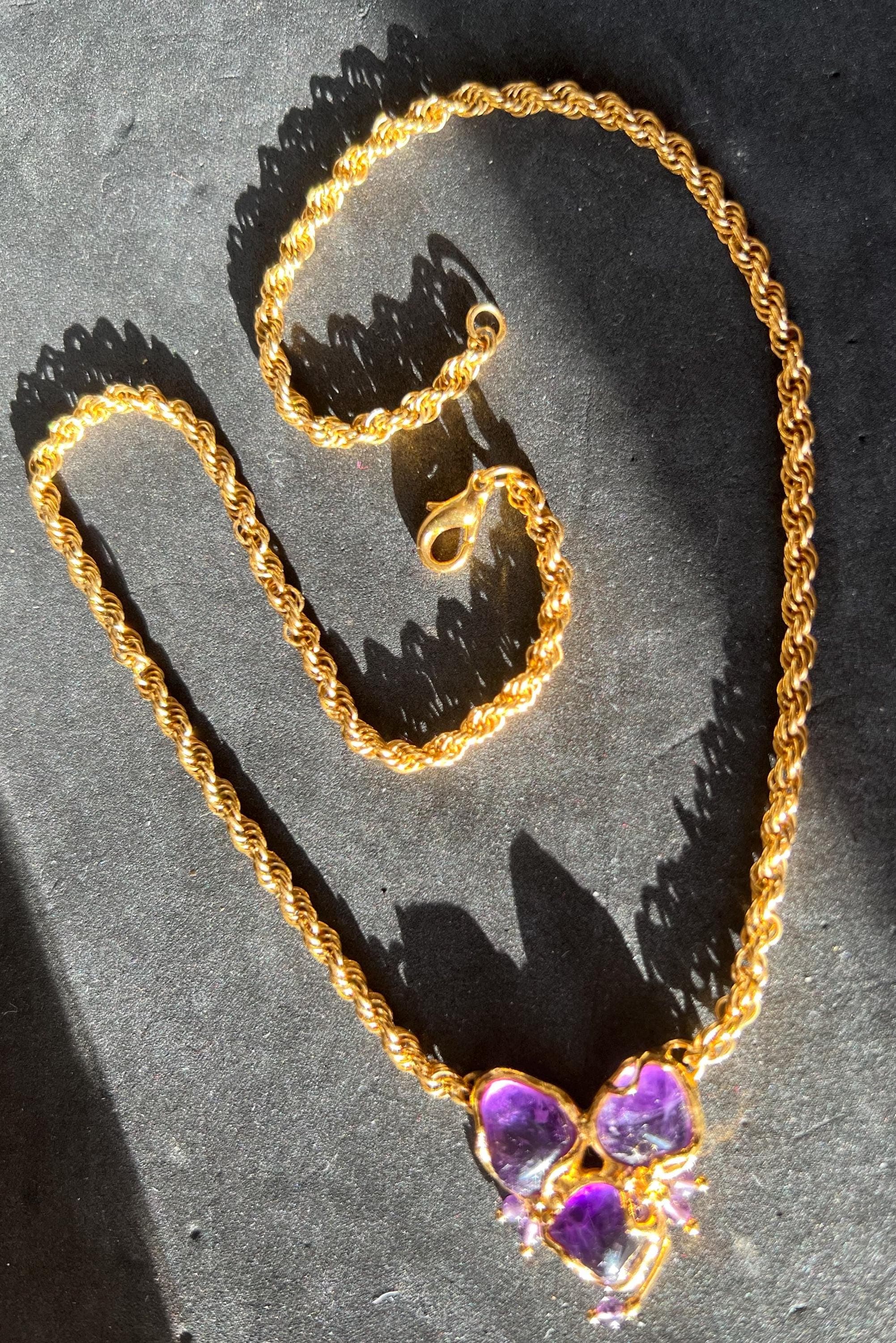 Product photo showing vintage 1990s gold-tone necklace with natural amethyst stones in a handcrafted pendant, feminine design. outdoor photo