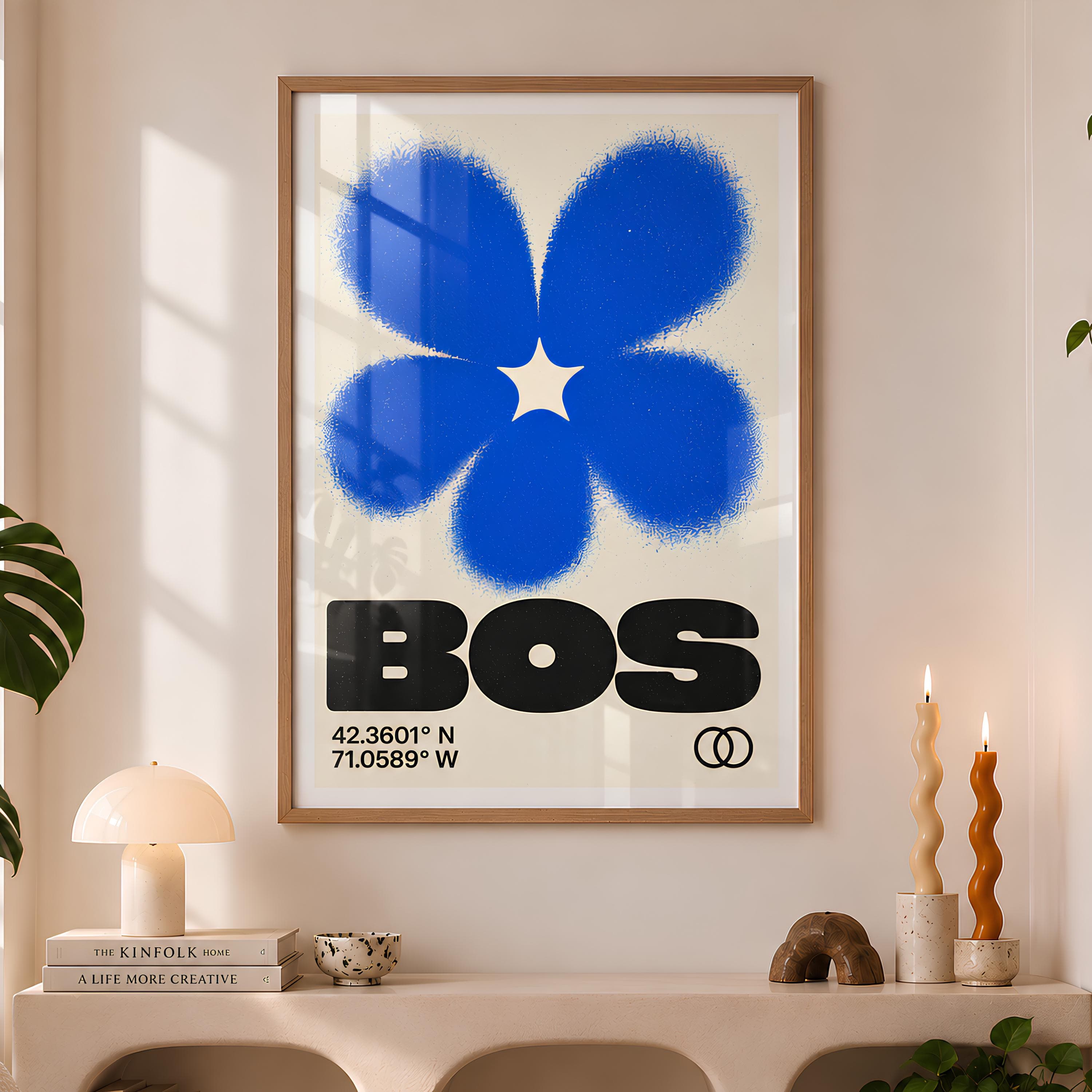 A framed wall art print featuring a large, textured blue flower graphic centered above the bold black text "BOS". Below the text, the coordinates "42.3601° N 71.0589° W" are printed in black, accompanied by a small black double-circle icon.