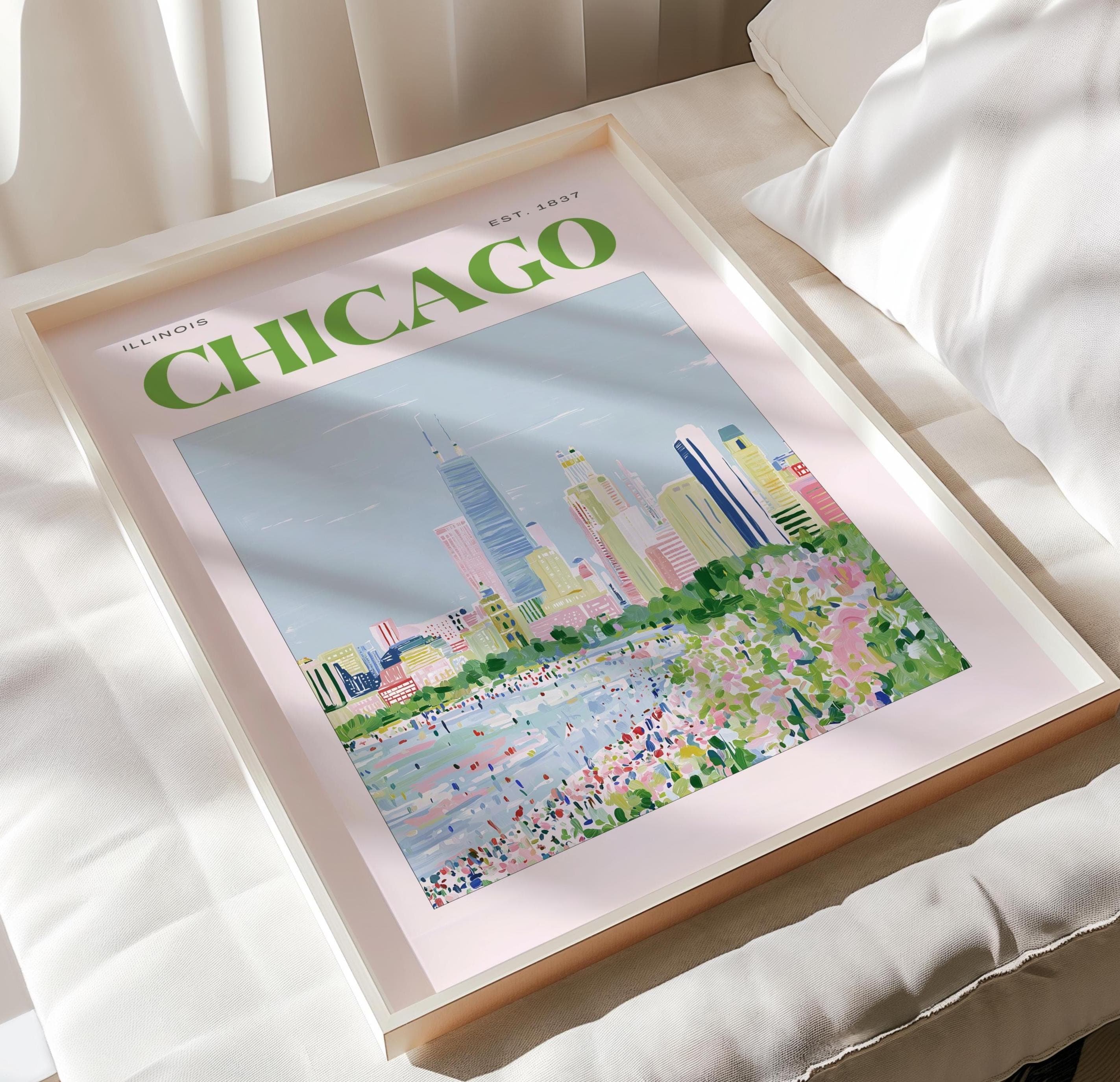 A framed art print featuring a stylized illustration of the Chicago skyline. The text CHICAGO is printed in large green letters at the top, with ILLINOIS and EST. 1837 in smaller font. The scene depicts colorful buildings and a park.