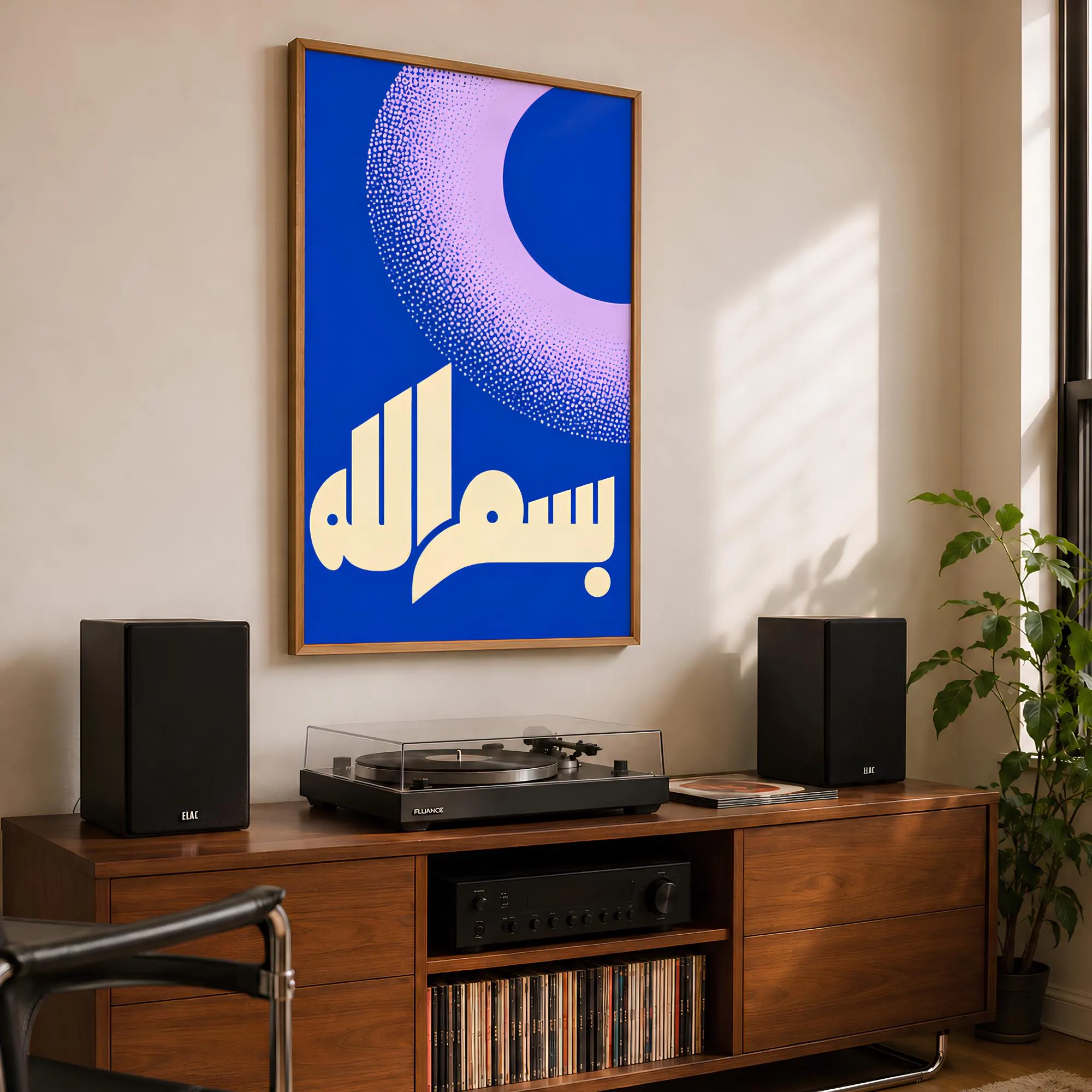 A rectangular wall art print in a wooden frame featuring a vibrant blue background with a large, pale pink crescent moon shape composed of stippled dots and the Arabic calligraphy for Bismillah in cream-colored lettering.