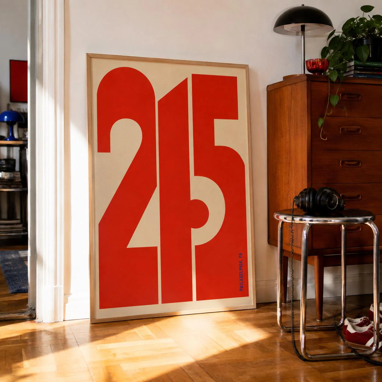 A rectangular framed wall art print featuring the large, bold red numbers 215 against a light beige background. The design uses thick, geometric typography. Small blue text reading PHILADELPHIA, PA is printed vertically in the lower right corner.